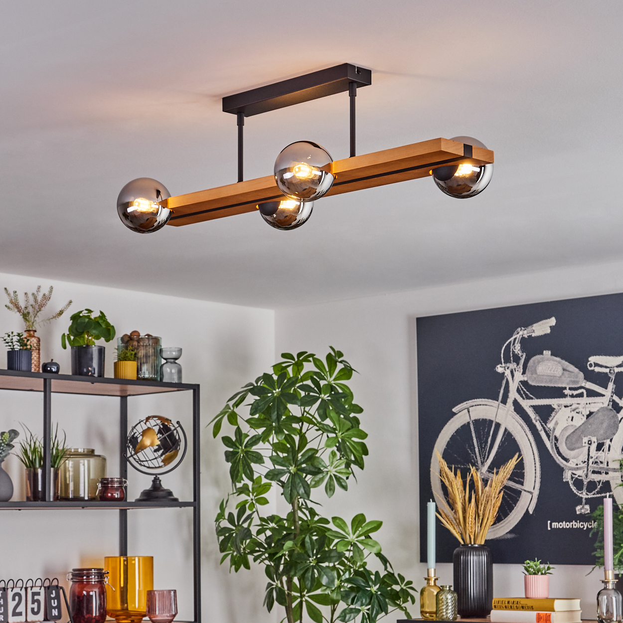 Eine moderne Deckenlampe mit vier Glaskugeln. Die Szene umfasst Pflanzen, Regale mit Dekoration und ein Motorrad-Kunstwerk.