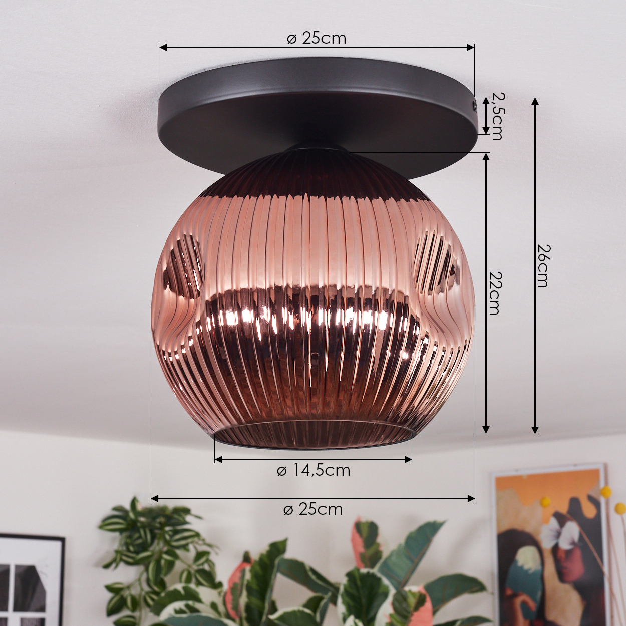 Kupferfarbene, gerippte, kugelförmige Deckenlampe mit schwarzem Sockel. Maße sind beschriftet. Pflanzen und ein gerahmtes Bild im Hintergrund.