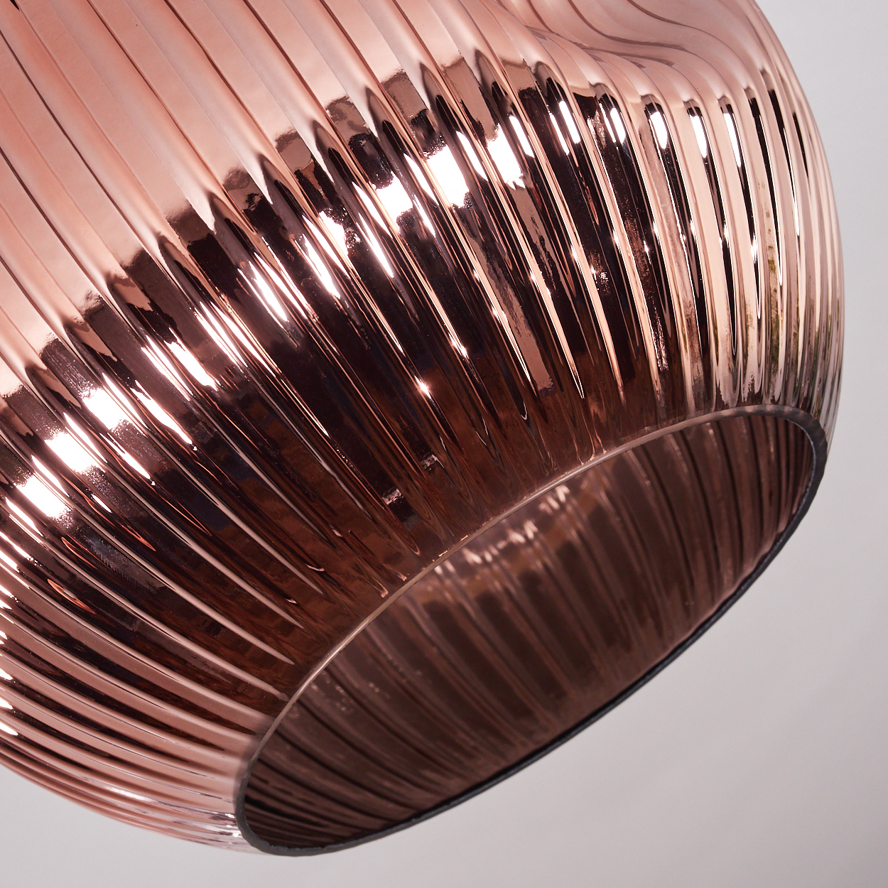 Nahaufnahme eines kupferfarbenen, geriffelten Glasschirms vor weißem Hintergrund. Die Reflexion zeigt Licht und die Form der Lampe.