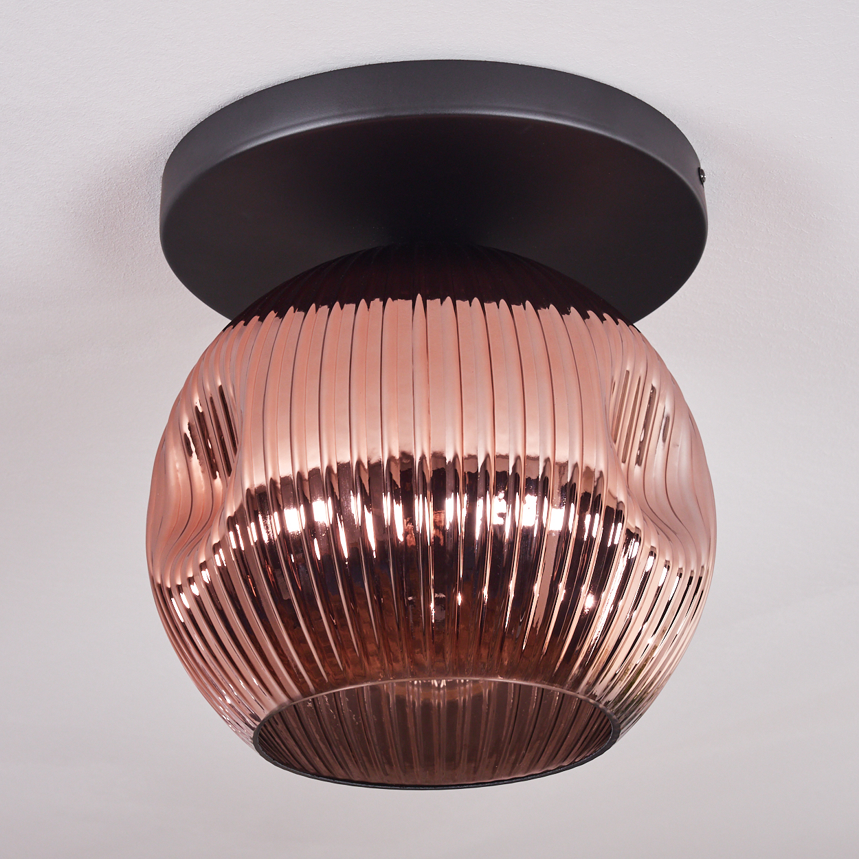 Eine kupferfarbene, gerippte Glas-Deckenlampe mit dunklem braunen Sockel ist an einer weißen Decke befestigt.