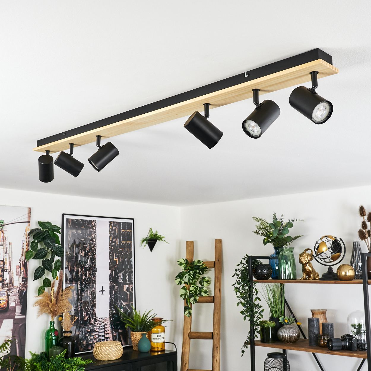 Ein modernes Interieur mit einer Deckenleuchte. Schwarze Strahler sind an einem Holzbalken montiert. Pflanzen und Dekor sind im Hintergrund.