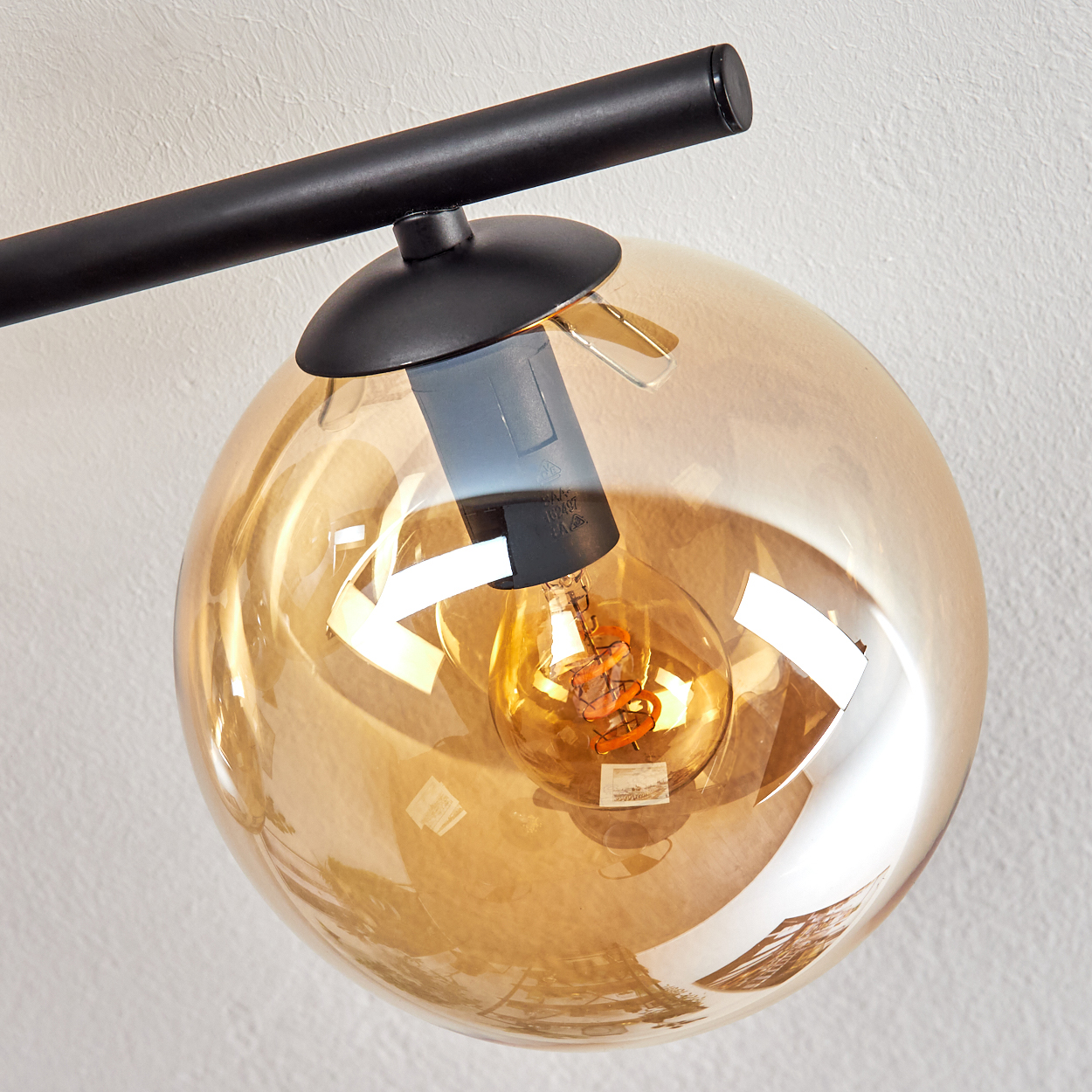 Nahaufnahme einer modernen Leuchte. Sie hat einen kugelförmigen, bernsteinfarbenen Glasschirm mit einer sichtbaren Glühbirne, die von einer schwarzen Metallstruktur gehalten wird.