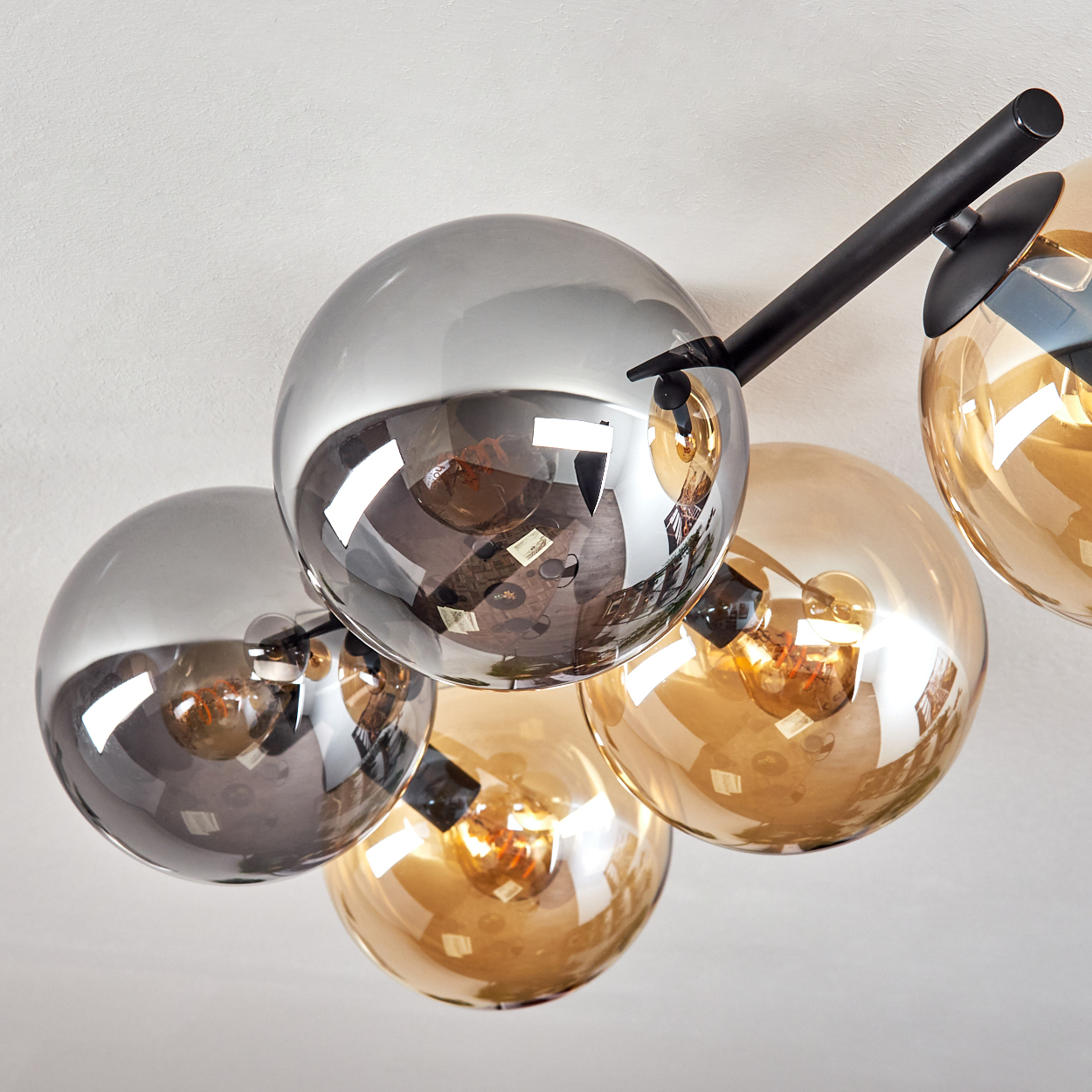 Eine moderne Deckenleuchte mit mehreren Glasglobus in Grau- und Bernsteinfarben, die das Licht reflektieren. Sie ist an einer weißen Decke befestigt.