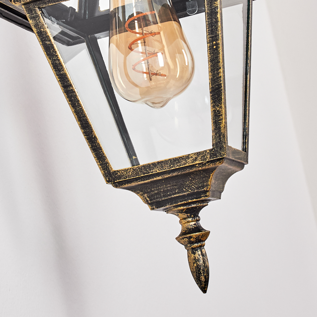 Nahaufnahme einer Vintage-Laterne. Sie hat ein Glasgehäuse und einen dekorativen, goldfarbenen Rahmen und eine leuchtende Glühbirne.