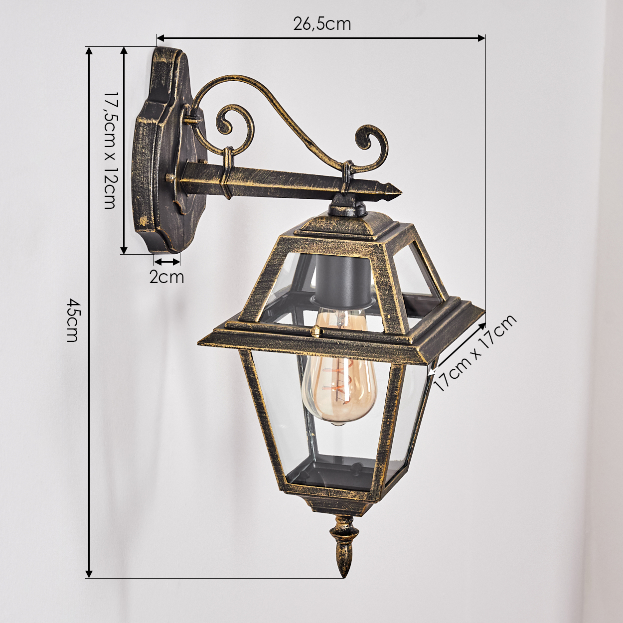 Eine verzierte, bronzefarbene Außenlampe ist an einer weißen Wand montiert. Abmessungen zeigen Größe und Form der Lampe.