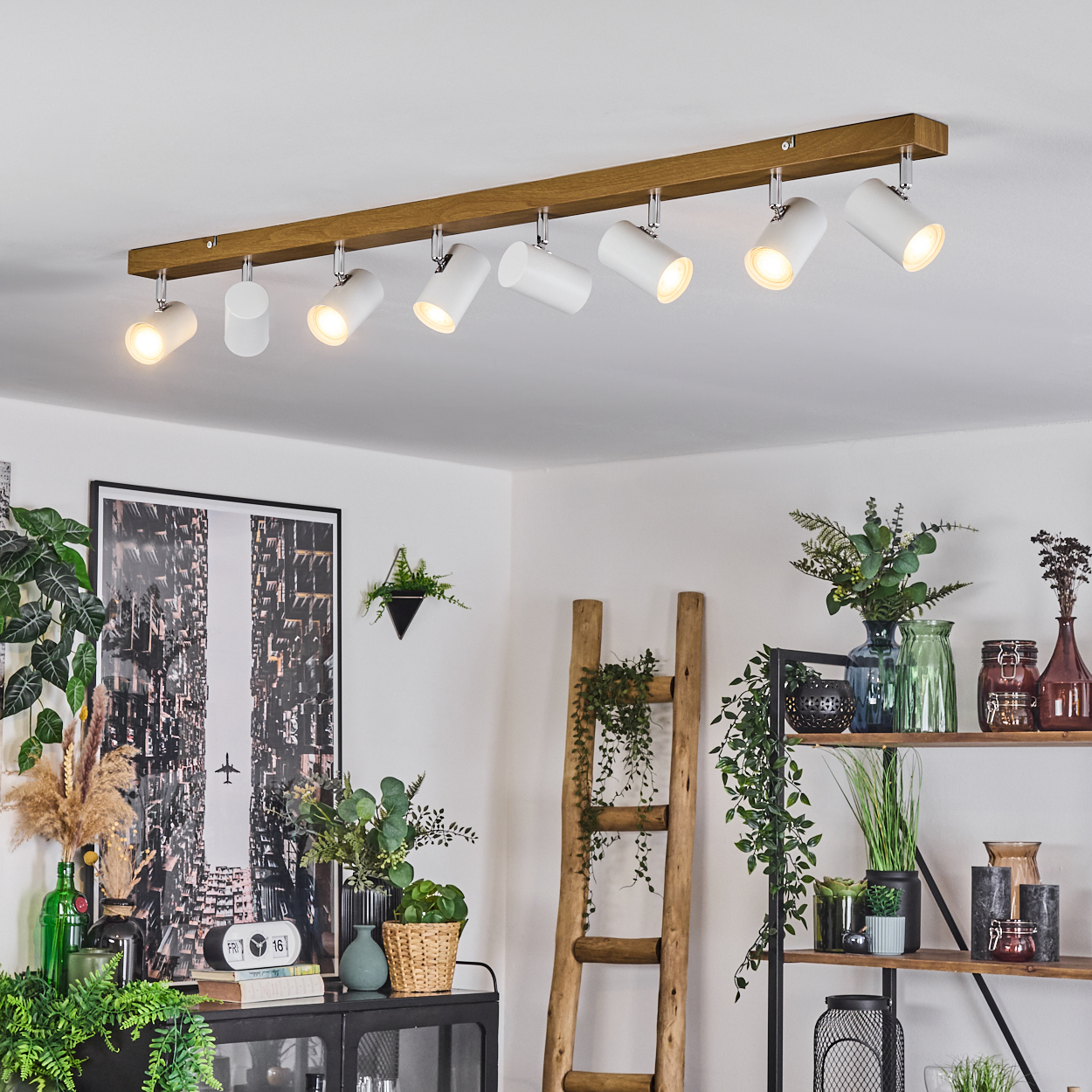 Eine moderne Deckenleuchte mit weißen Strahlern. Eine Holzleiter, Pflanzen und Kunst im Raum schaffen eine gemütliche Atmosphäre.