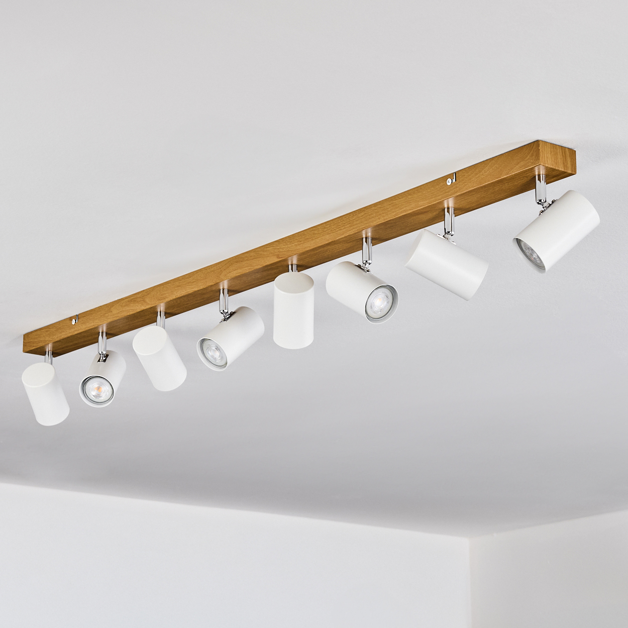 Ein Holzbalken mit acht weißen Strahlern. Die Lichter sind abgewinkelt. Der Hintergrund ist eine weiße Decke.