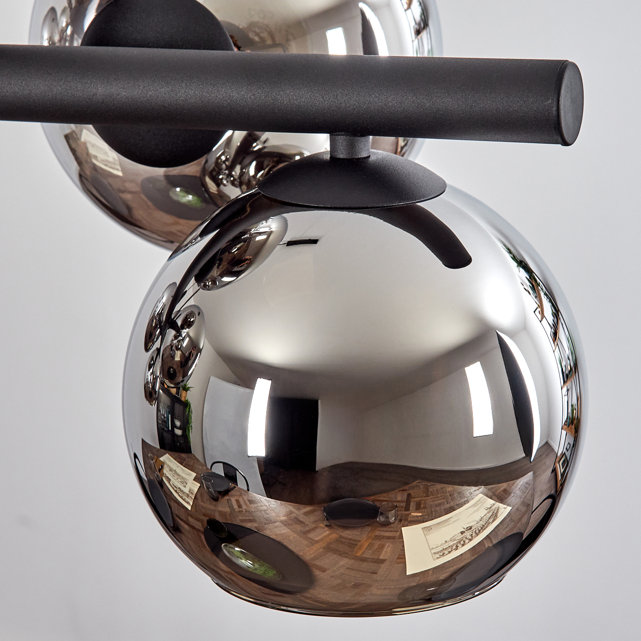 Eine verchromte Kugellampe reflektiert einen Raum mit Holztisch, Stühlen und weißer Wand. Die Lampe ist schwarz und hat einen schwarzen Balken.