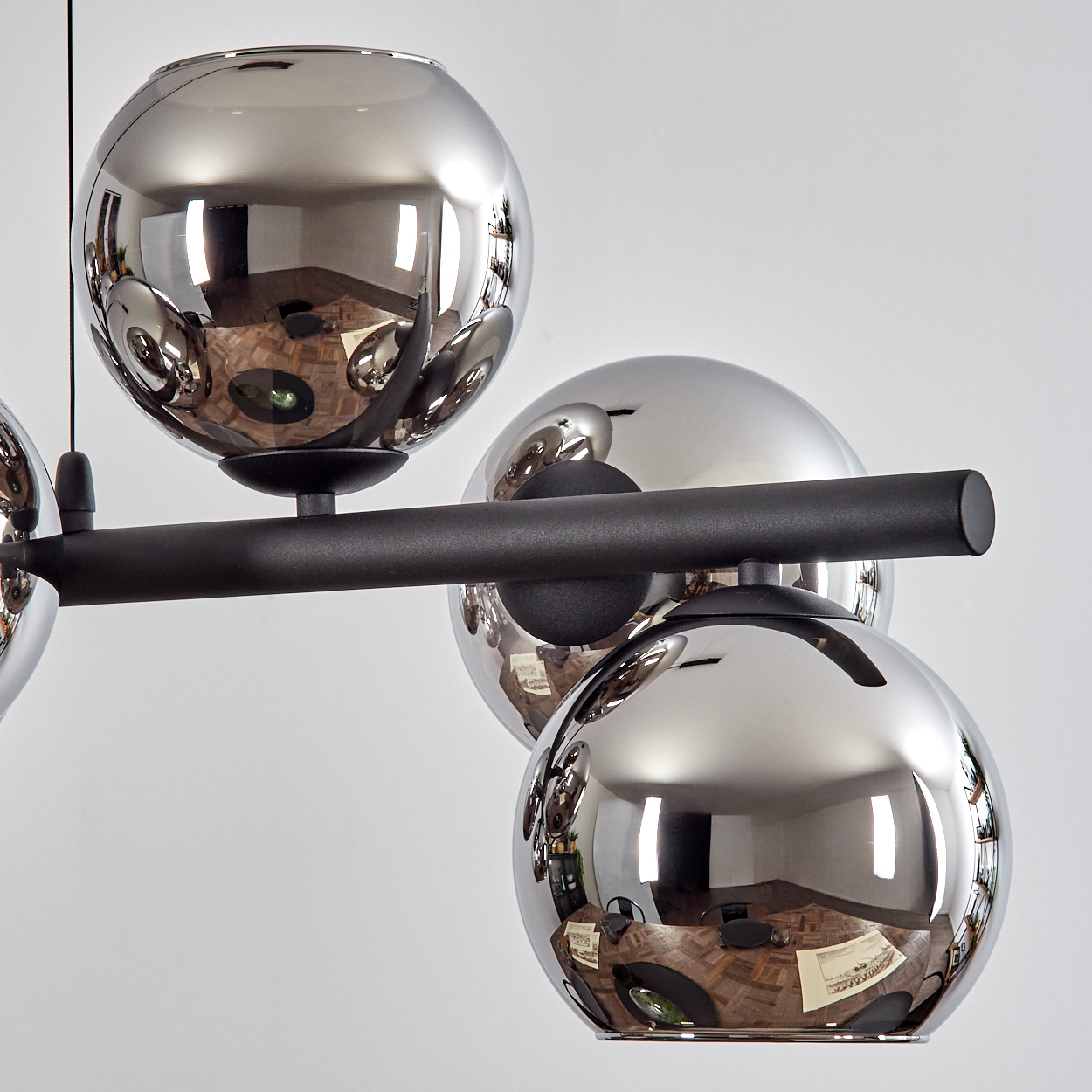 Eine moderne Deckenleuchte mit mehreren reflektierenden Chromkugeln. Die Kugeln sind auf einem schwarzen Balken vor weißem Hintergrund montiert.