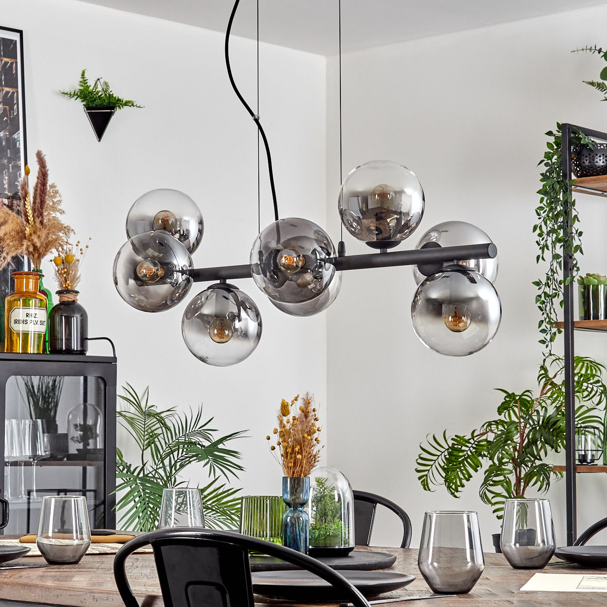 Ein Esszimmer mit Holztisch, schwarzen Stühlen und einem modernen Kronleuchter. Pflanzen und dekorative Vasen schmücken das Dekor.