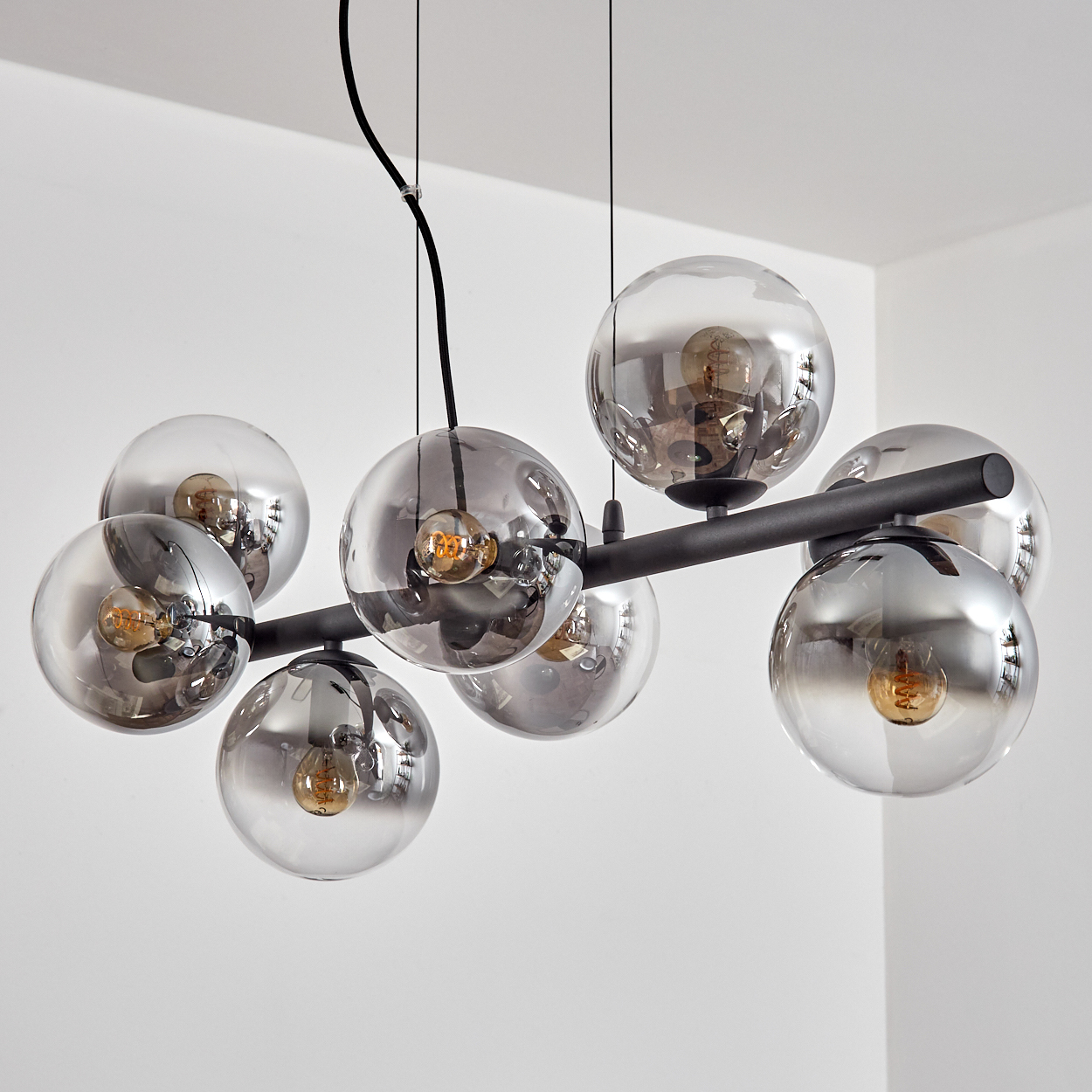 Eine moderne Hängelampe mit acht rauchigen Glaskugeln, jede mit einer Glühbirne, hängt von der Decke. Die Halterung ist schwarz.