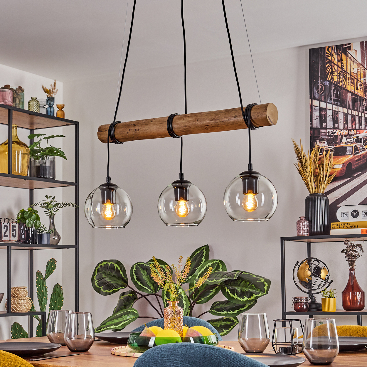 Esszimmer mit Holztisch, Hängelampen und verschiedenen Dekorationen, darunter Pflanzen, Gläser und ein Bild.