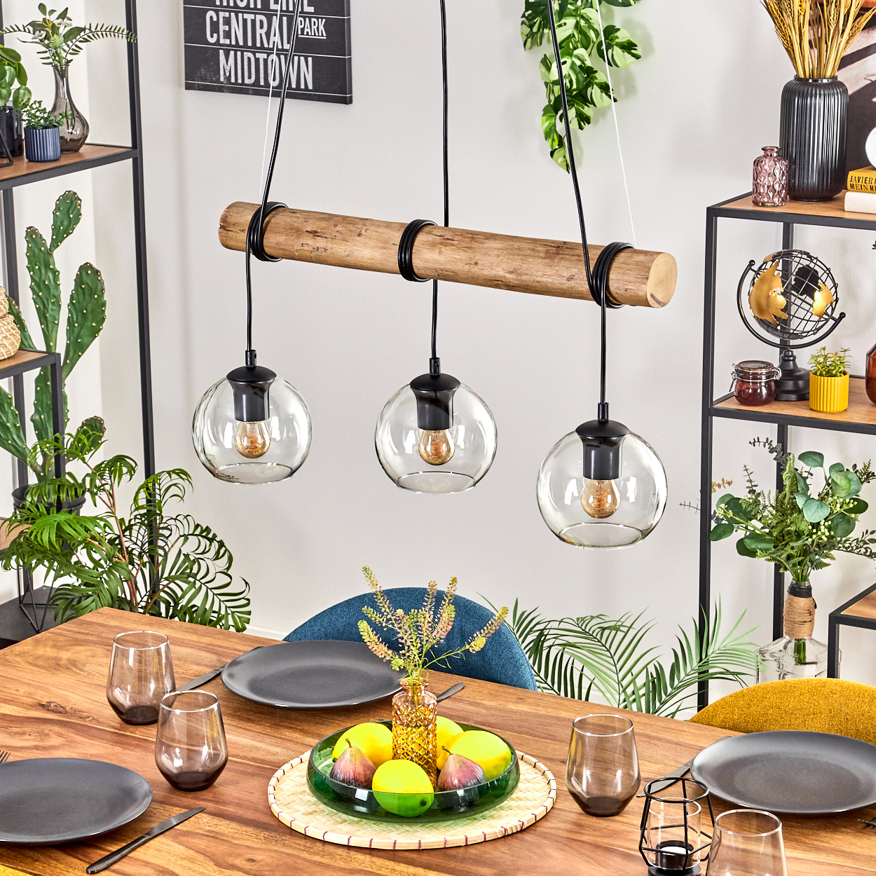 Esstisch mit drei Kugelleuchten, Obst und Tellern. Pflanzen und Dekoration im Hintergrund. Holztisch.