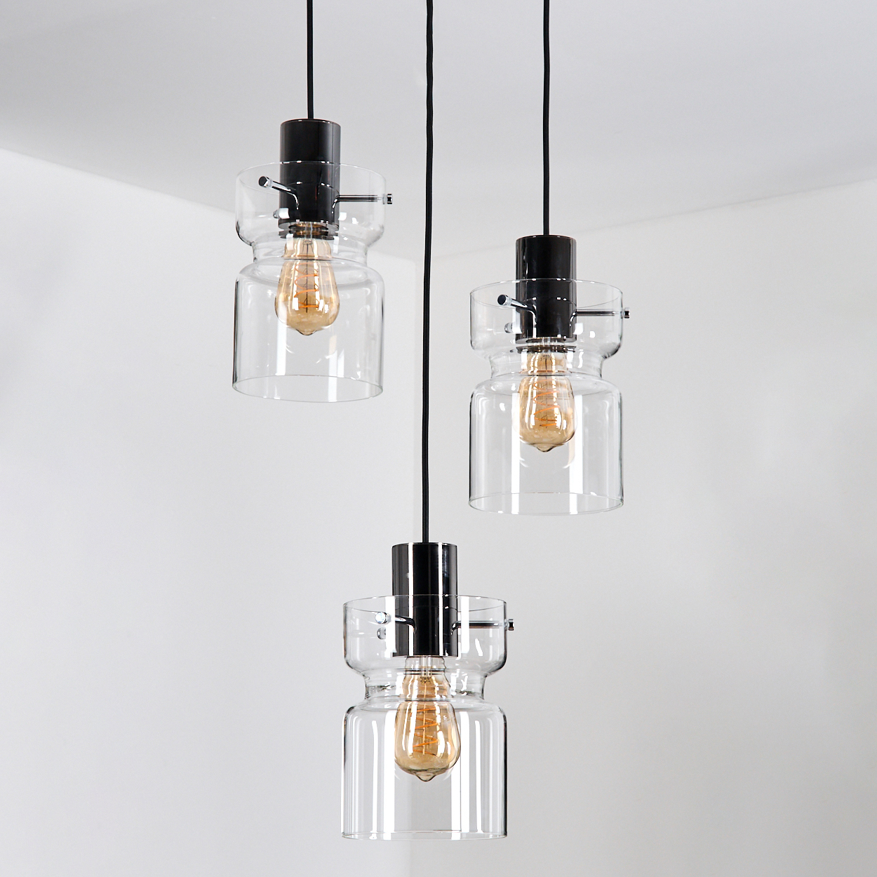 Drei Pendelleuchten mit Glasschirmen und Edison-Glühbirnen hängen vor einem weißen Hintergrund von der Decke.