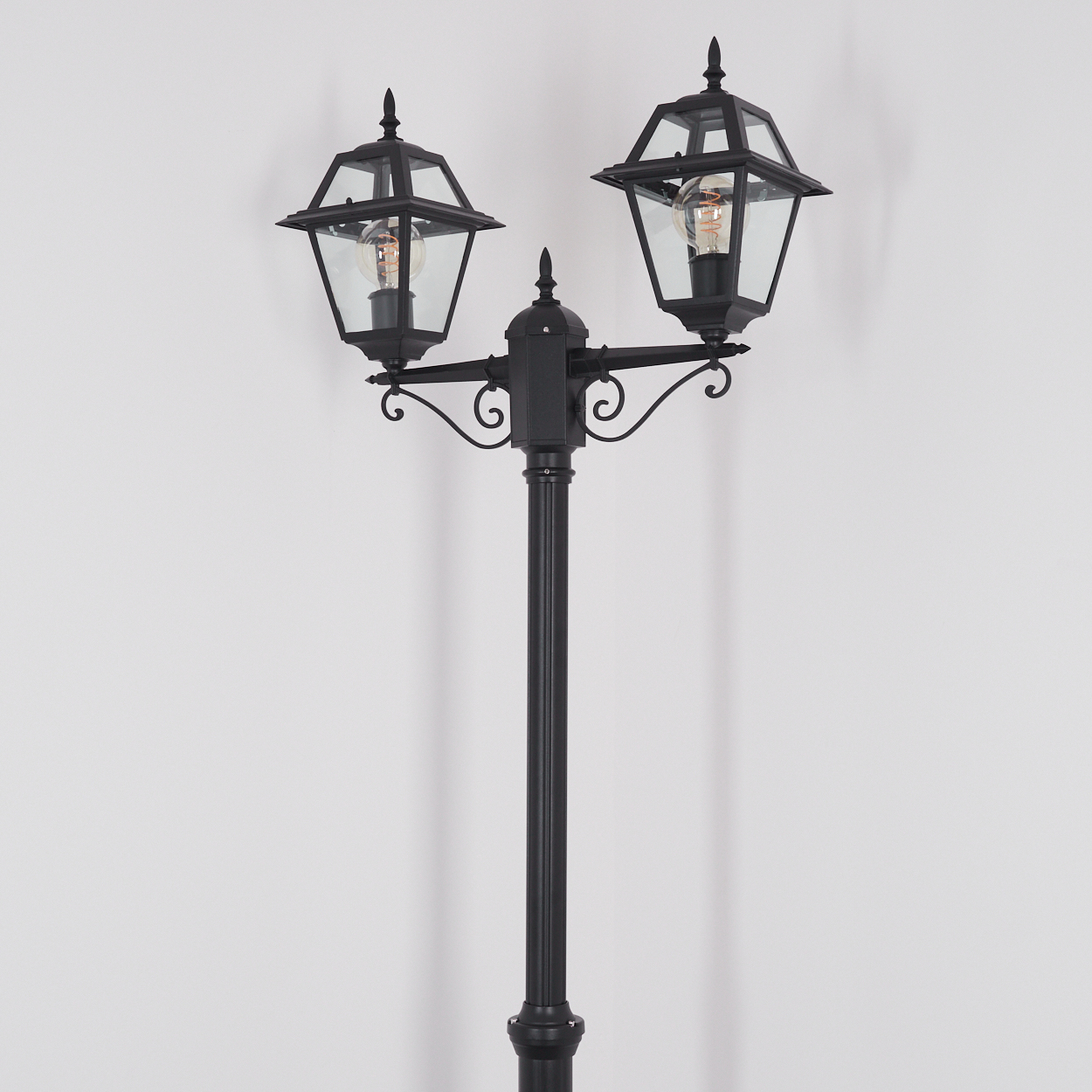 Eine schwarze Laternenpfahl mit zwei Lampen an der Spitze. Jede Lampe hat die Form einer Laterne mit Glasfront und einer Glühbirne.