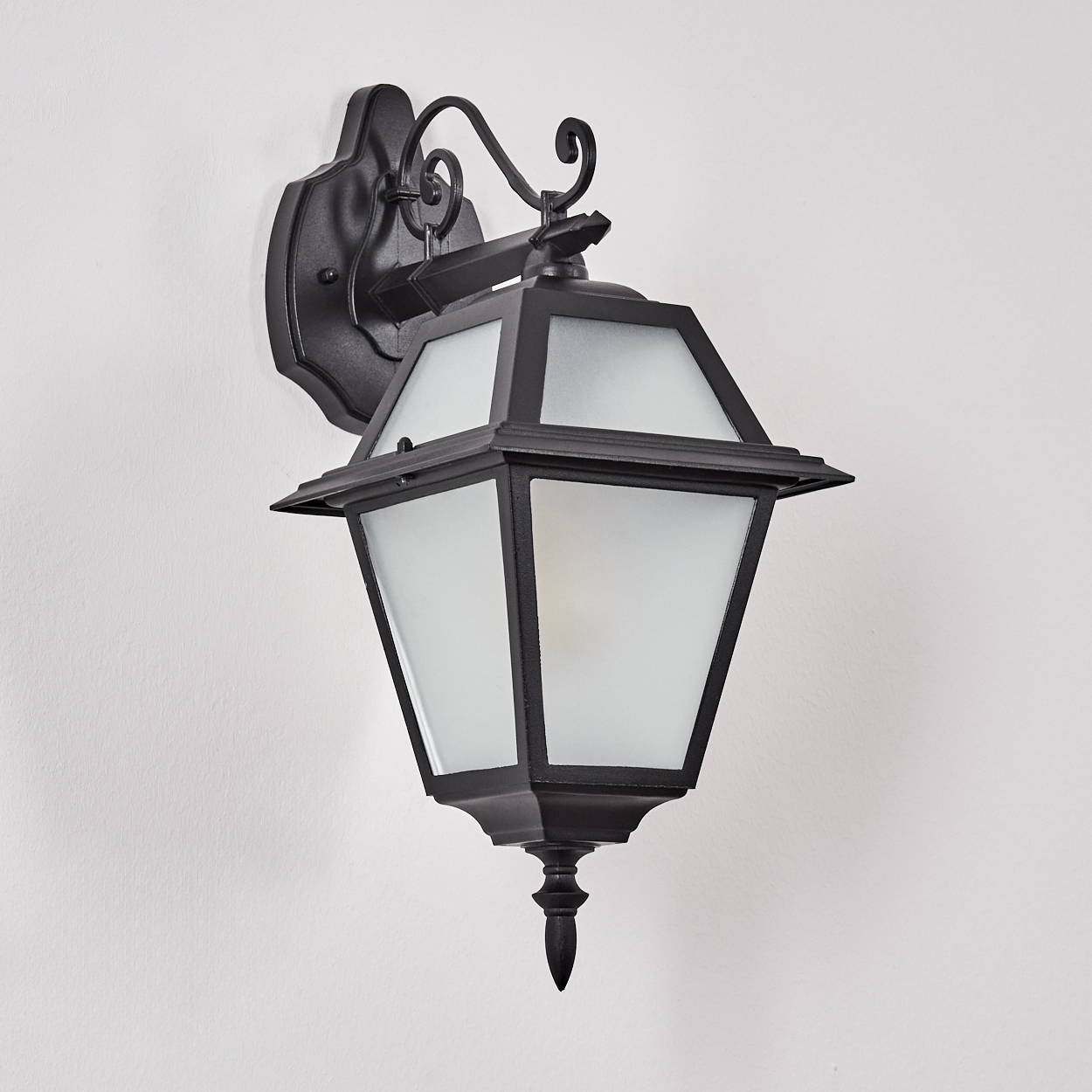Eine schwarze, verzierte Außenwandleuchte mit mattierten Glasscheiben ist an einer weißen Wand befestigt.