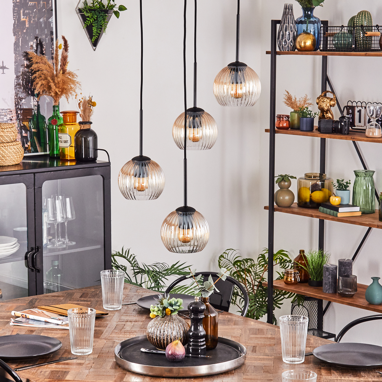 Esszimmer mit Holztisch, Hängelampen, Tellern, Gläsern und Dekorationsgegenständen auf Regalen und Schränken.