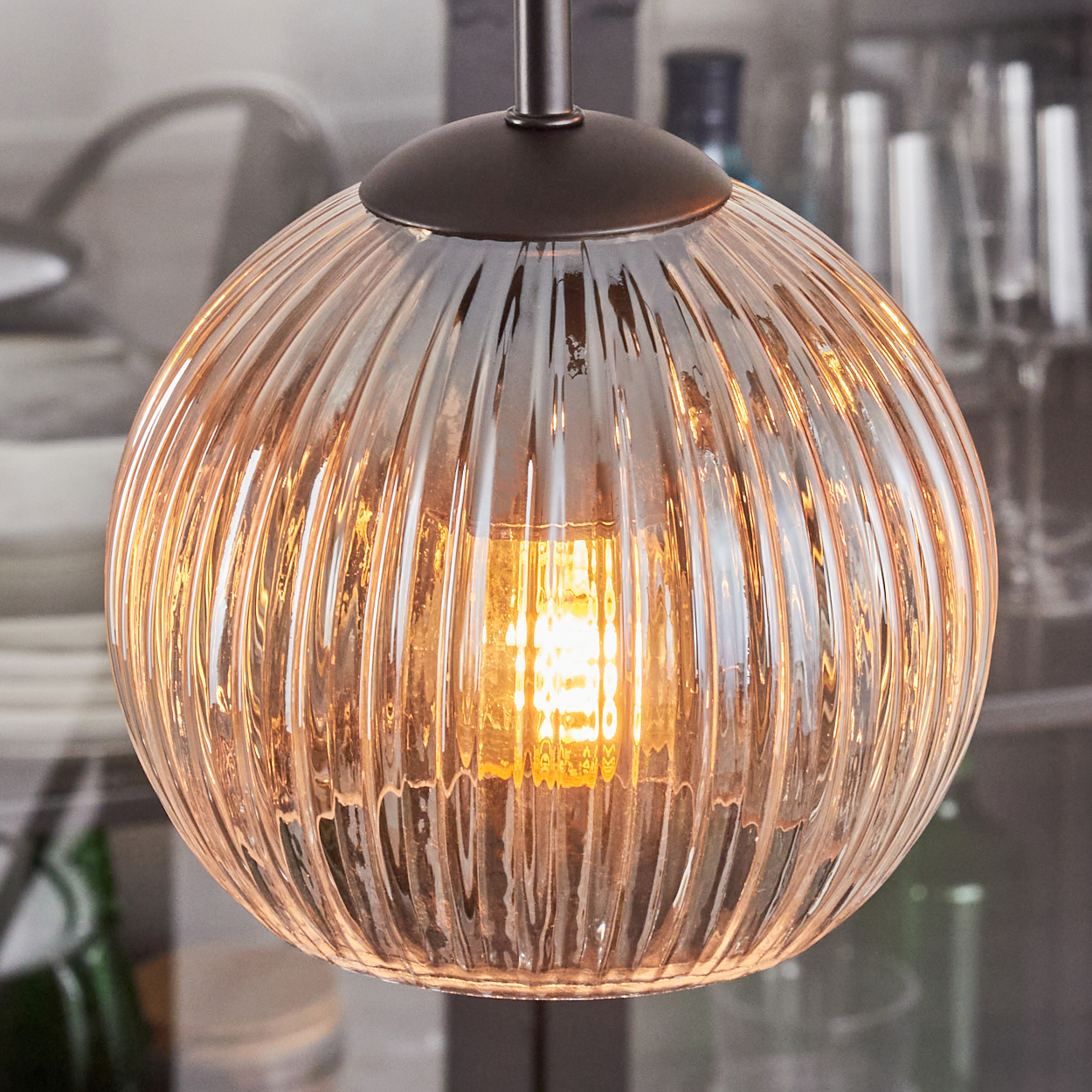 Nahaufnahme einer Glas-Pendelleuchte mit geripptem Design. Das Licht ist an und strahlt warm, mit dunkler Metallbefestigung.