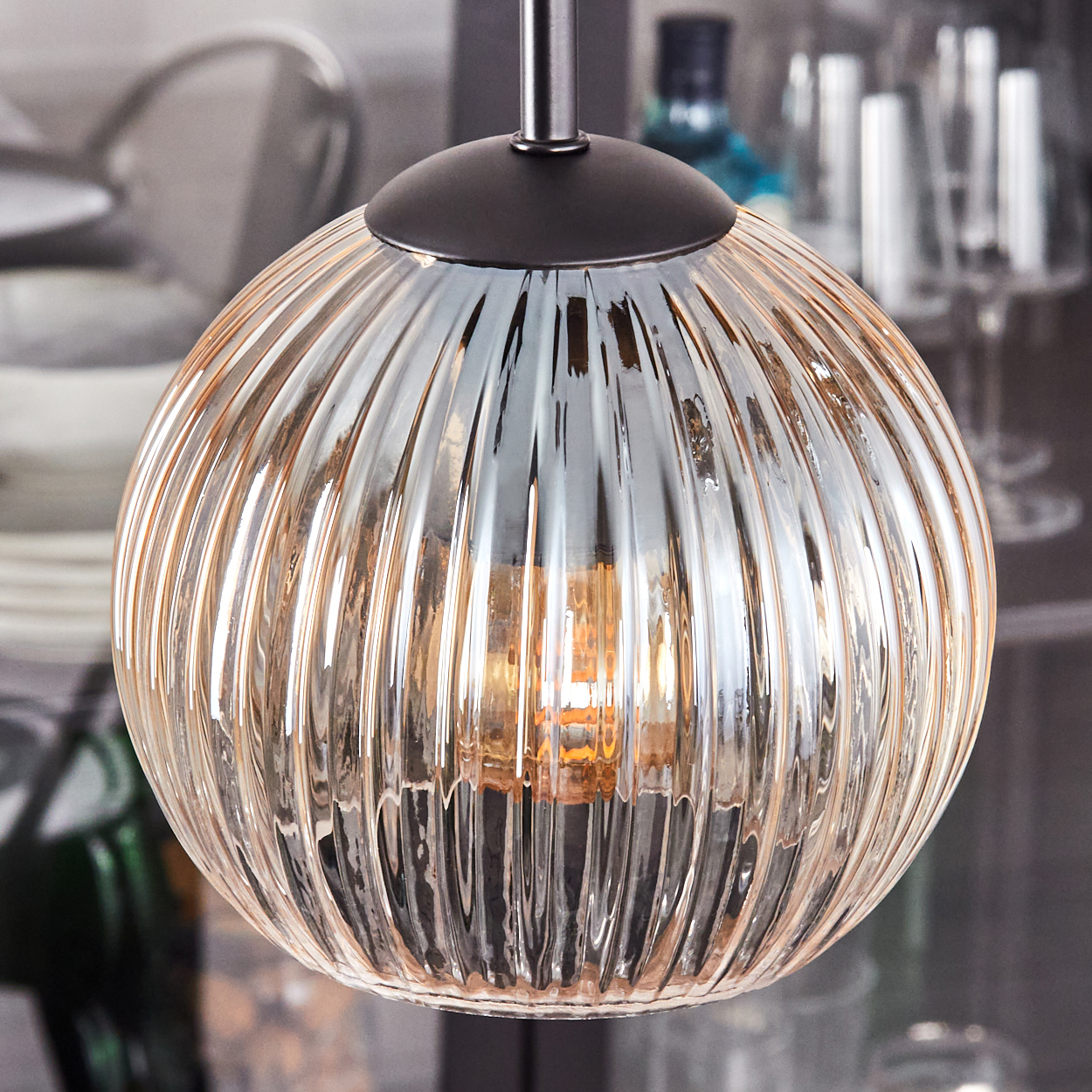Nahaufnahme einer Glas-Pendelleuchte mit geripptem Design. Die Lampe ist von innen beleuchtet und hat einen warmen, orangefarbenen Schein.