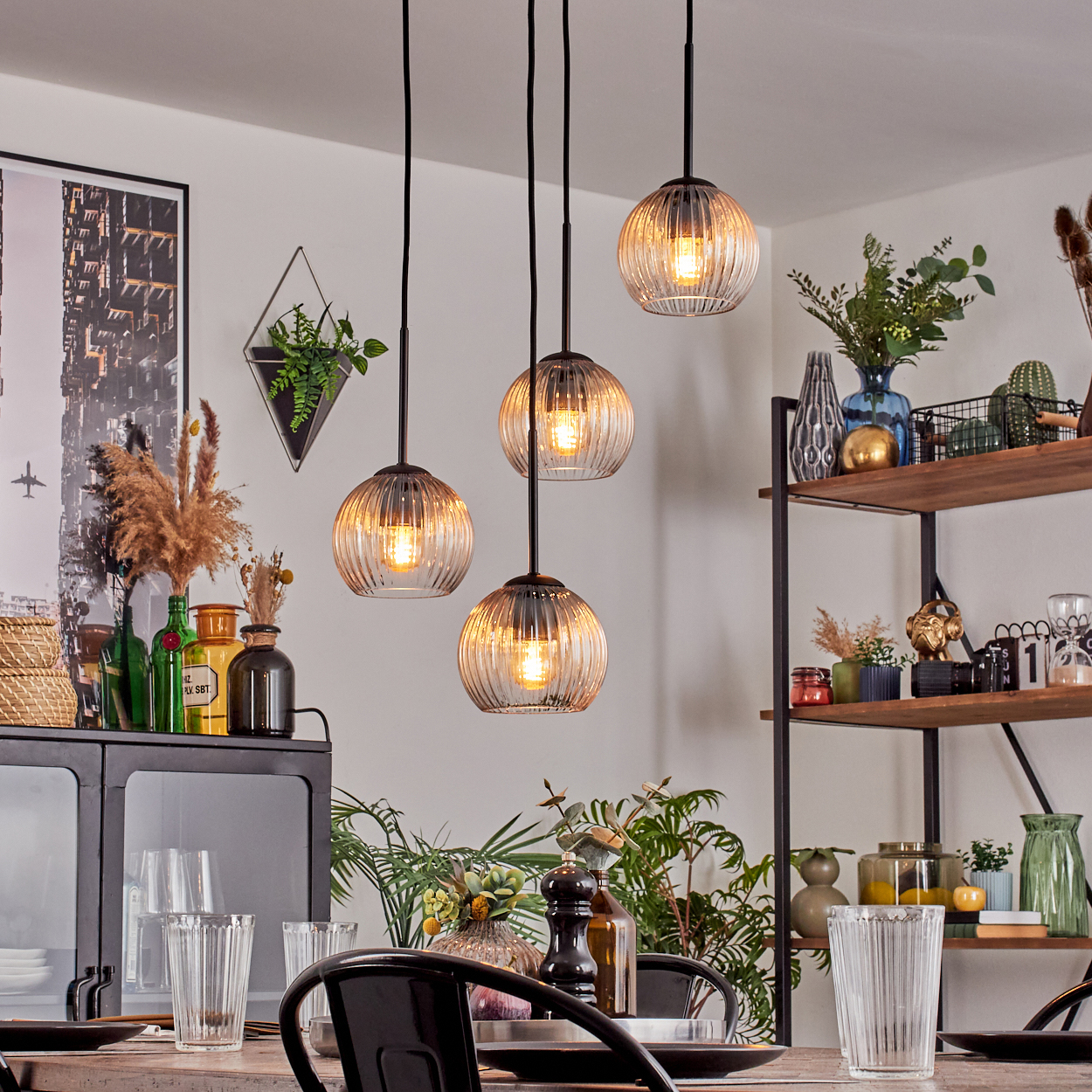 Esszimmer mit Hängelampen. Tisch mit Gläsern gedeckt. Regale mit Dekorationen. Schwarze Stühle und Schrank. Pflanzen und Vasen.
