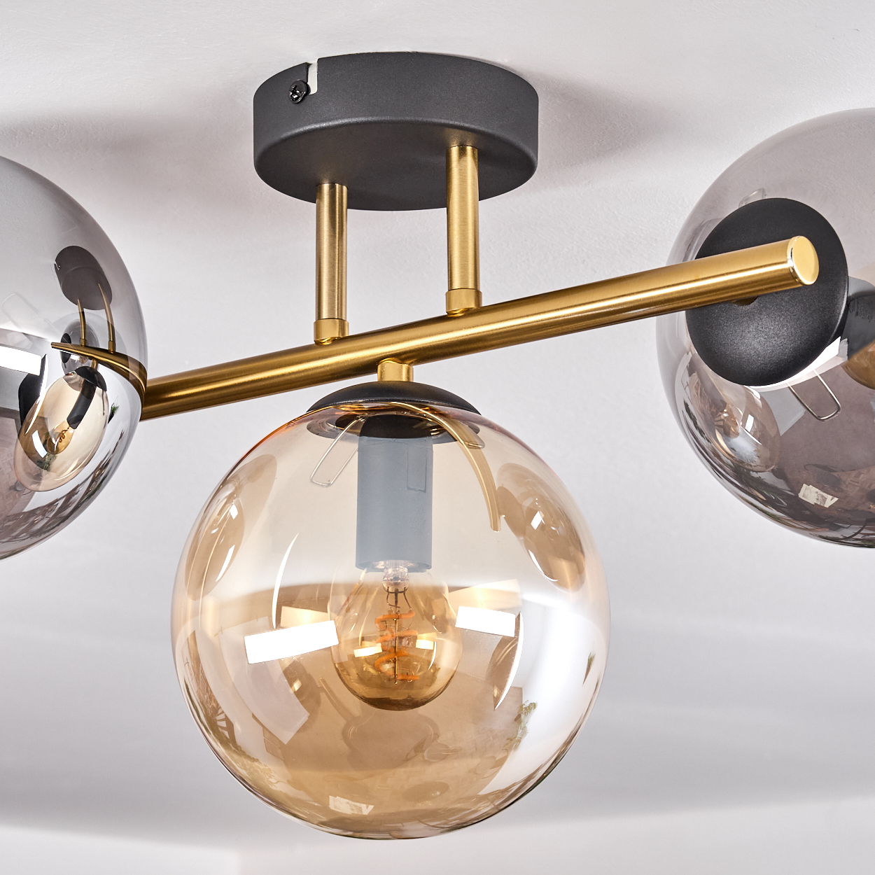 Moderne Deckenleuchte mit drei Glaskugelschirmen. Die Leuchte hat einen goldfarbenen Arm und einen schwarzen Sockel, mit weißer Decke.