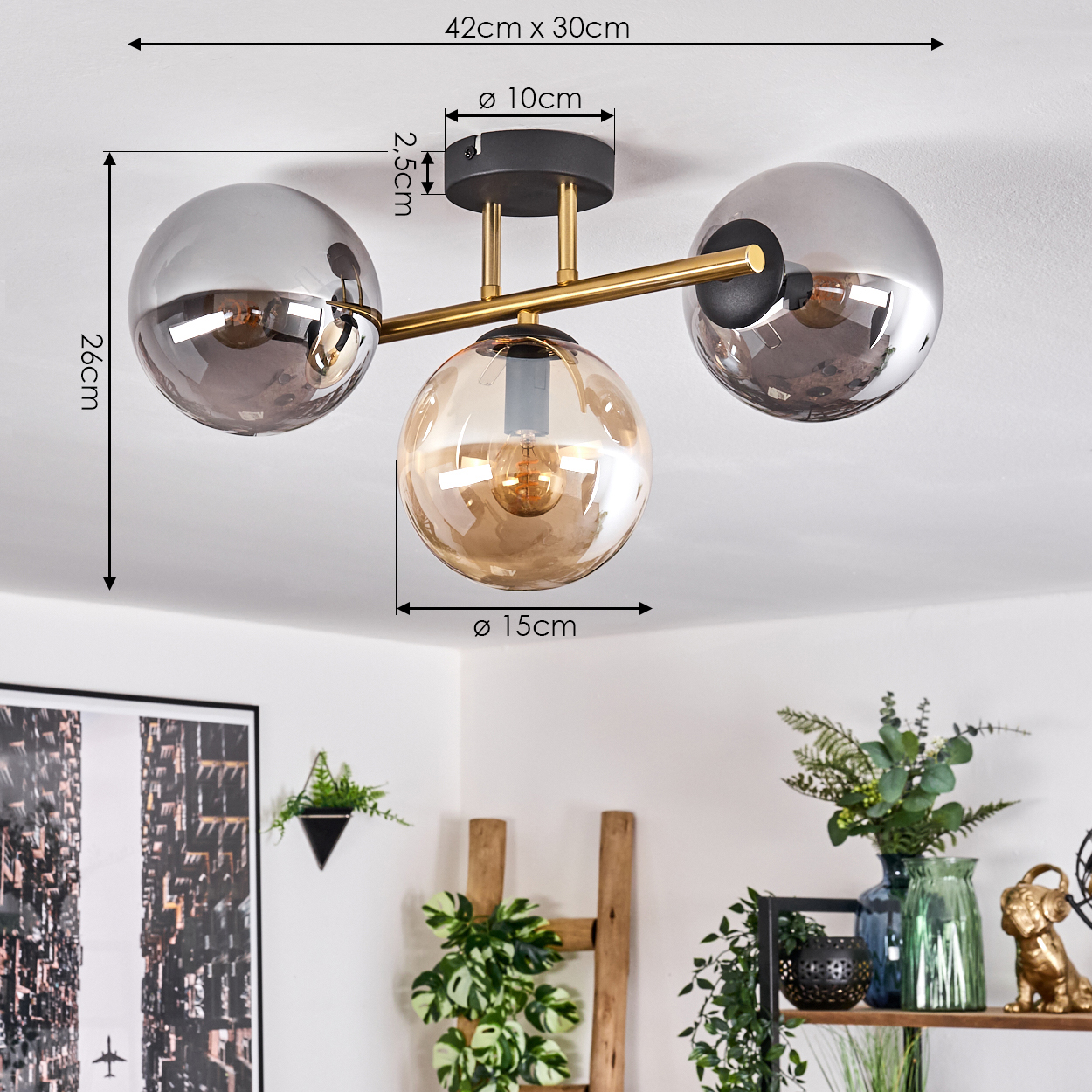 Moderne Deckenlampe mit drei Glaskugeln. Maße beschriftet. Im Hintergrund ein Regal mit Deko und Pflanzen.