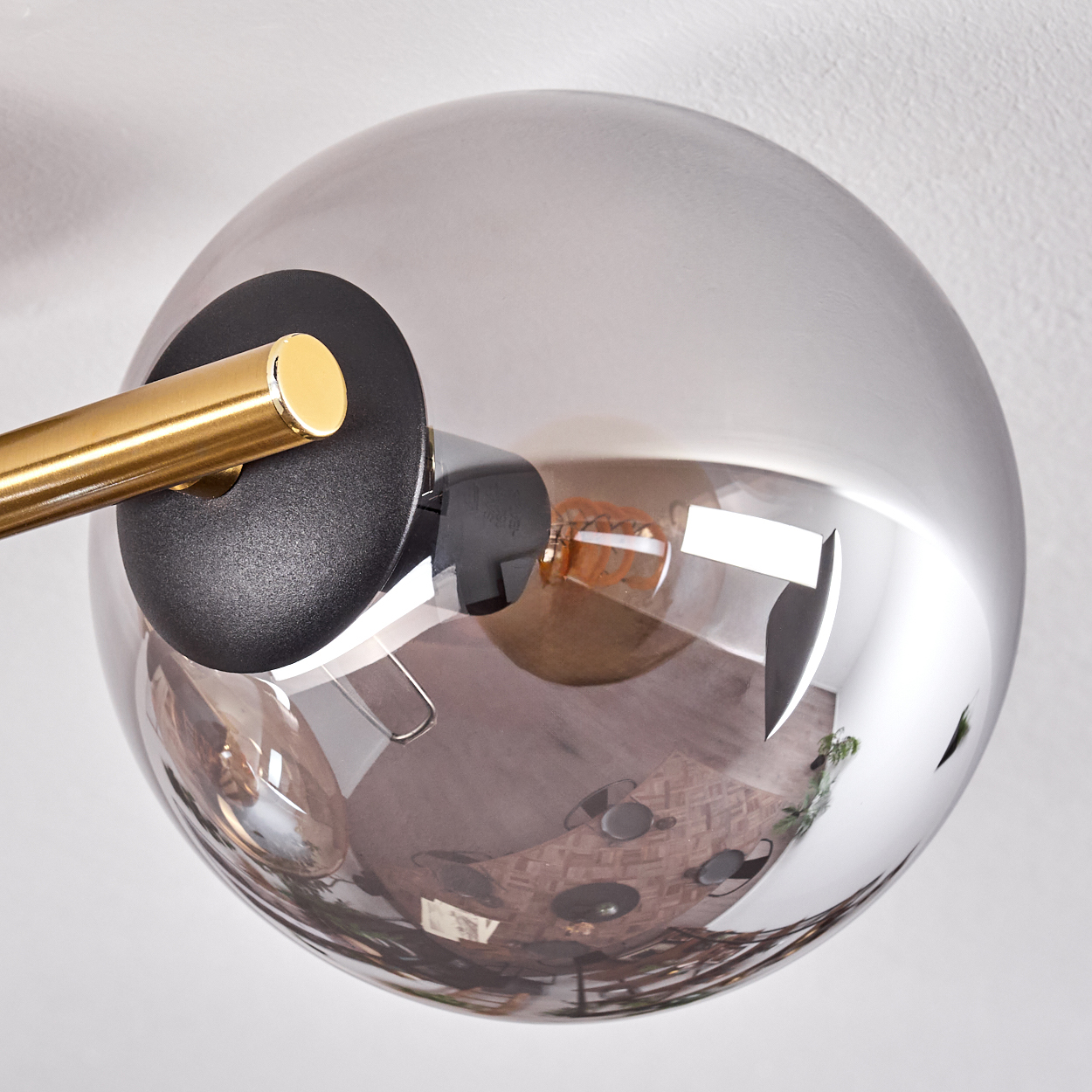 Eine moderne Lampe mit einer reflektierenden Glaskugel. Ein goldfarbener Arm und eine schwarze Halterung sind an der Kugel befestigt.