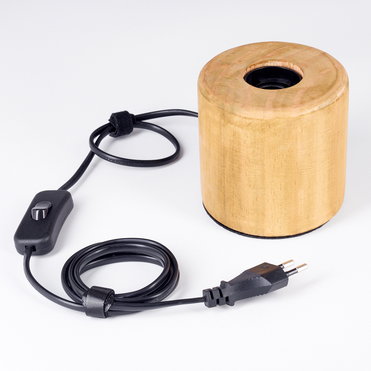 Ein Holzzylinder mit einem schwarzen Loch oben. Ein schwarzes Kabel mit Schalter und Stecker ist angeschlossen. Weißer Hintergrund.