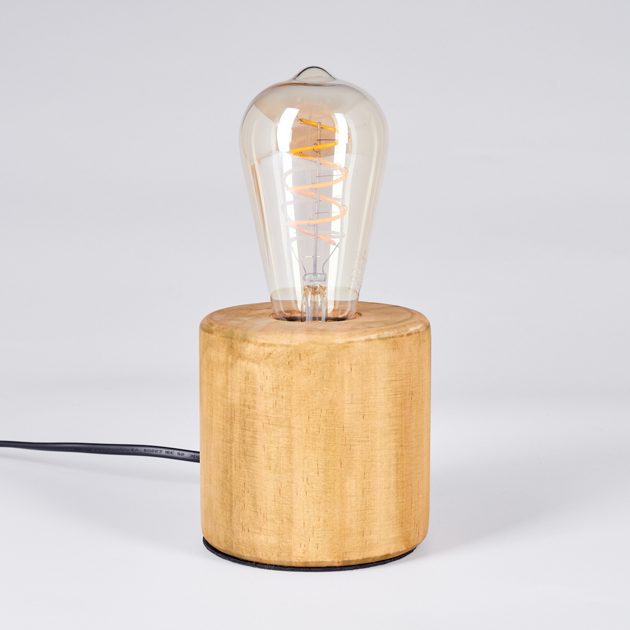 Eine Holzlampen mit einer großen Glühbirne. Die Birne ist klar mit einem Wendelfaden. Der Sockel ist zylindrisch und aus Holz.
