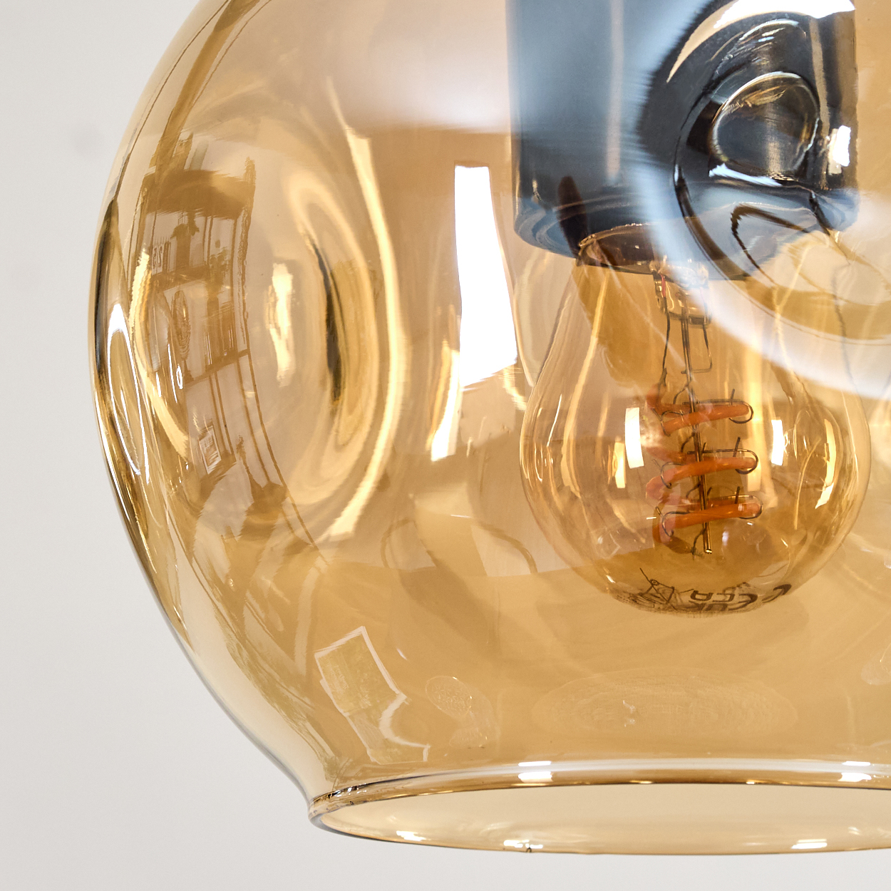 Nahaufnahme einer Glasleuchte. Das Glas ist bernsteinfarben und umgibt eine Glühbirne mit sichtbarem Glühfaden. Der Hintergrund ist weiß.
