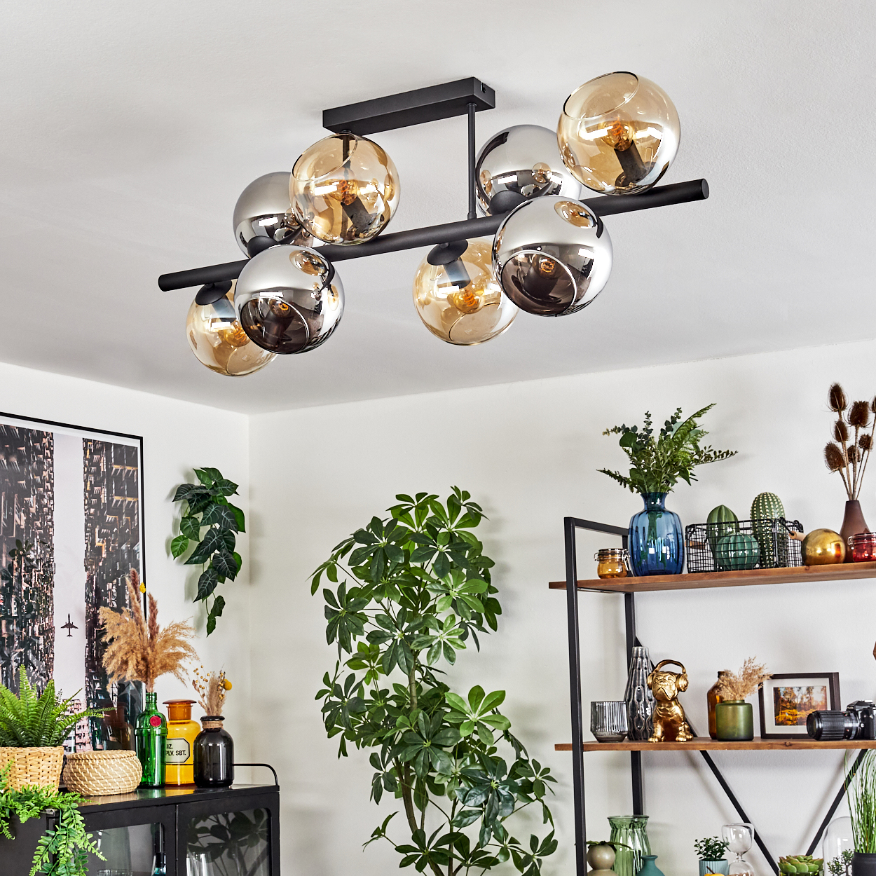 Ein modernes Wohnzimmer mit einem schwarzen Kronleuchter, Pflanzen und Dekorationsgegenständen auf einem Regal. Der Kronleuchter hat Glaskugeln.
