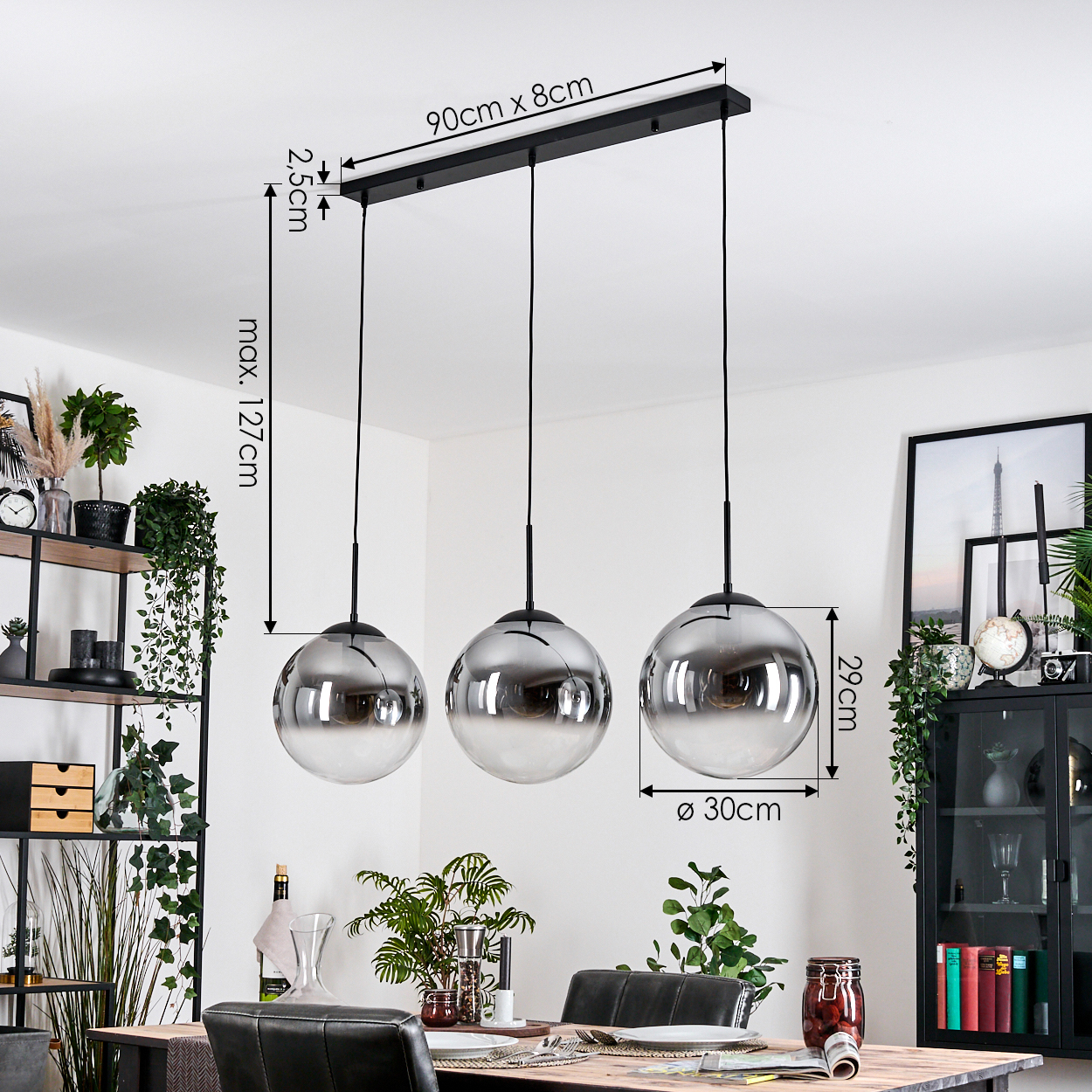 Ein modernes Esszimmer mit drei kugelförmigen Pendelleuchten. Die Lichter hängen über einem Holztisch, im Hintergrund Pflanzen.