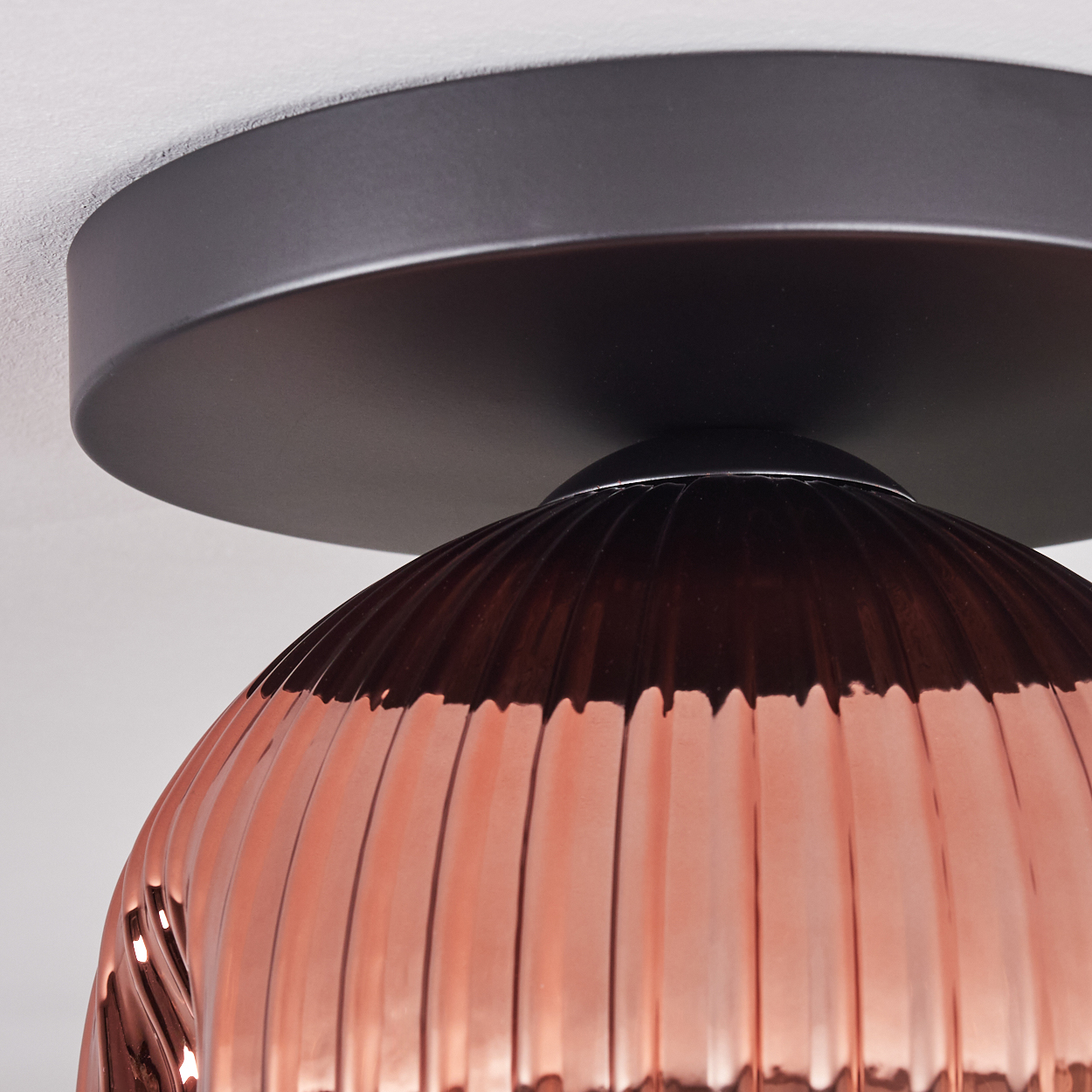 Nahaufnahme einer Deckenlampe. Sie hat einen bronzefarbenen Glasschirm mit vertikalen Rippen. Der Sockel ist schwarz und kreisförmig.