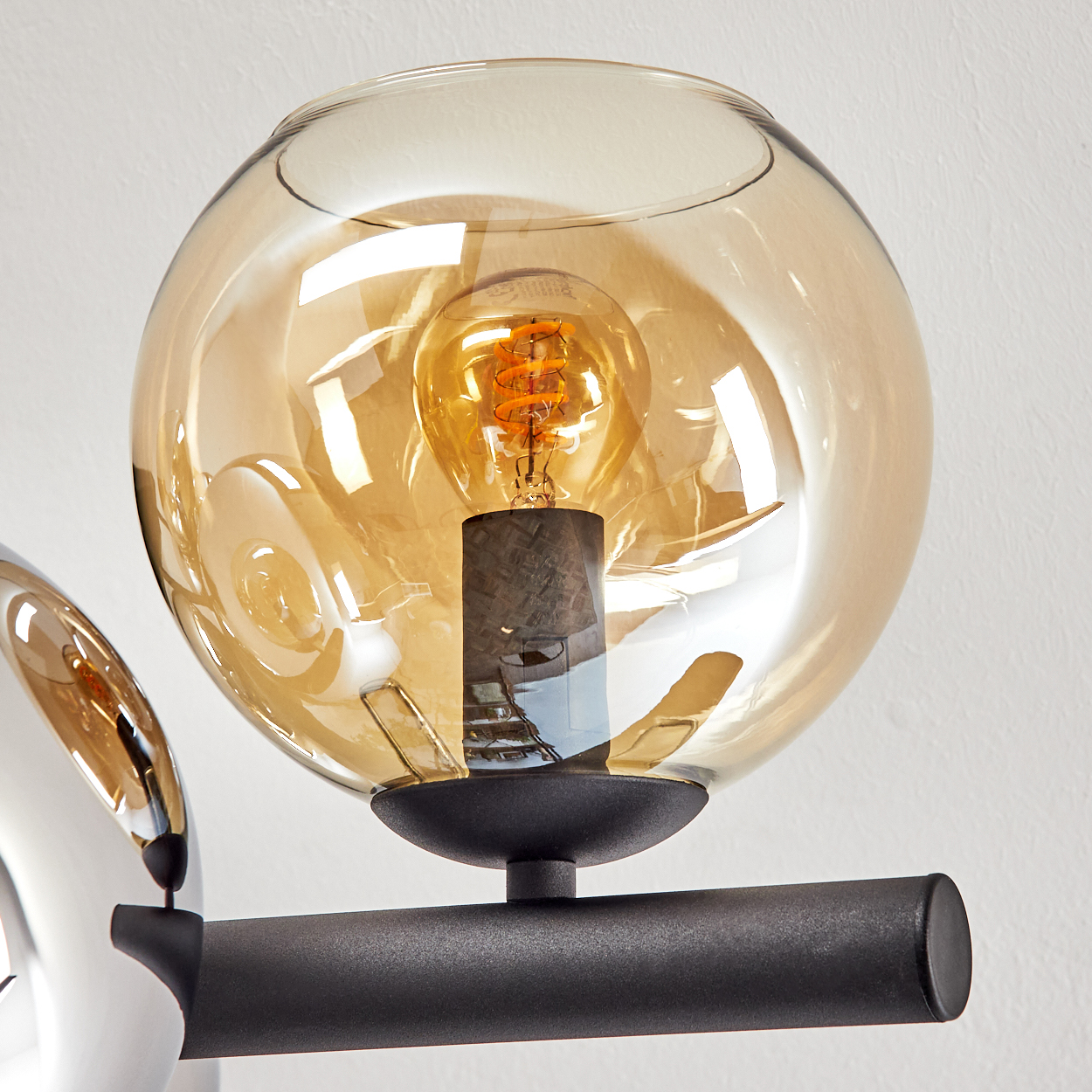 Nahaufnahme einer Leuchte mit Glaskugel. Im Inneren befindet sich eine Glühbirne. Die Leuchte hat einen schwarzen Metallarm.