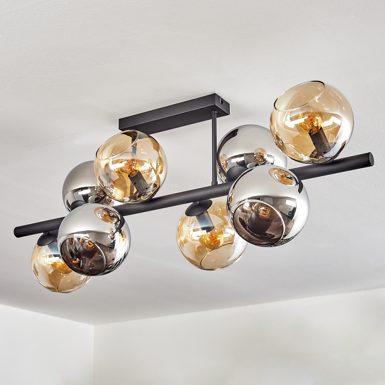 Moderne Deckenleuchte mit kugelförmigen Glühbirnen. Einige sind verchromt, andere bernsteinfarben. Die Halterung hat schwarze Metallstangen und eine weiße Decke.
