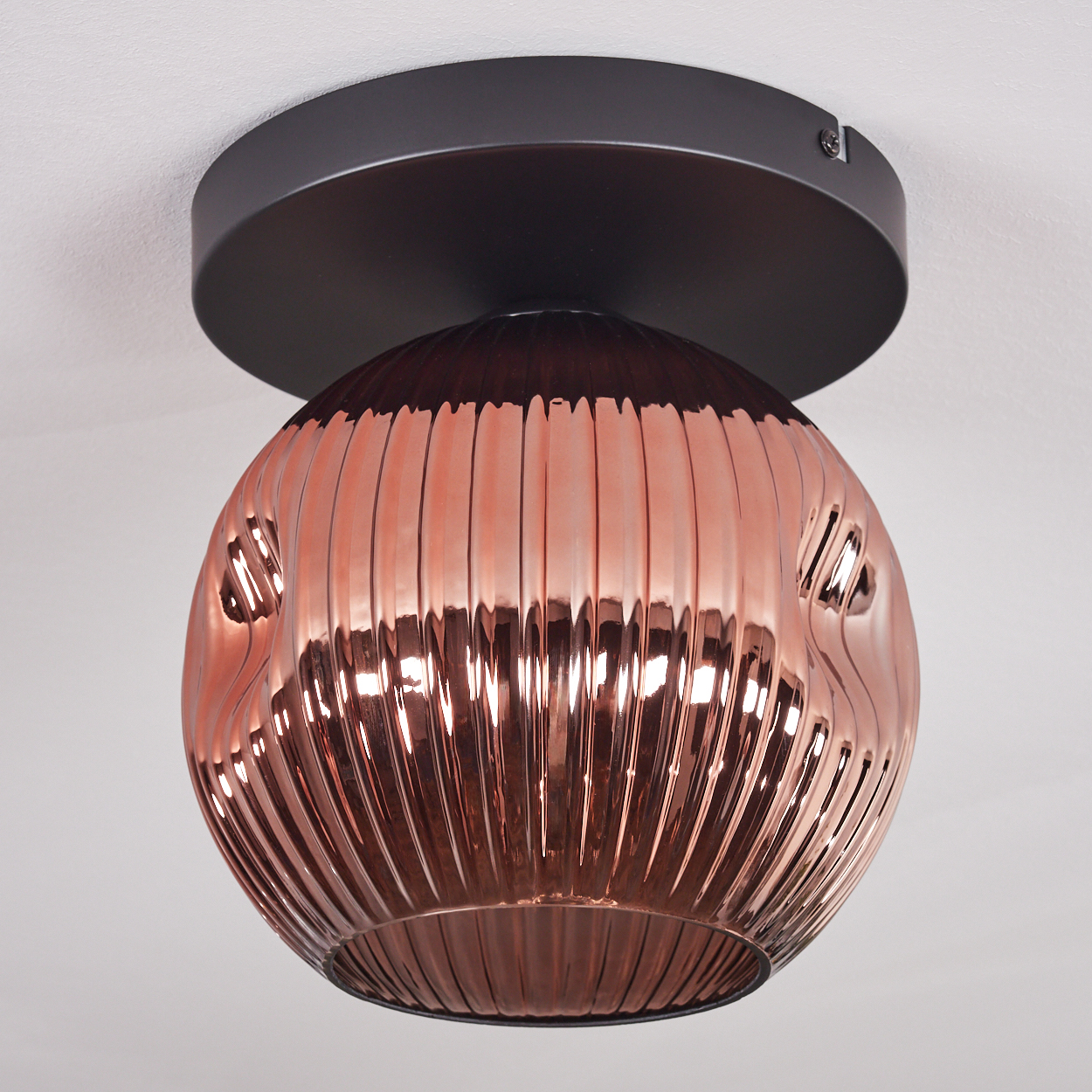 Eine moderne, kupferfarbene Deckenlampe aus Glas mit geriffelter Oberfläche. Sie hat einen kreisförmigen schwarzen Sockel und ist an einer weißen Decke montiert.