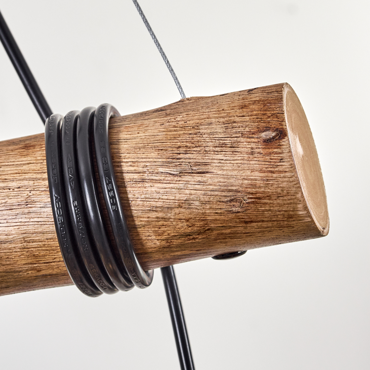 Nahaufnahme eines Holzbalkens mit schwarzen Kabeln. Ein Metallkabel und schwarze Metallstangen sind ebenfalls vorhanden.