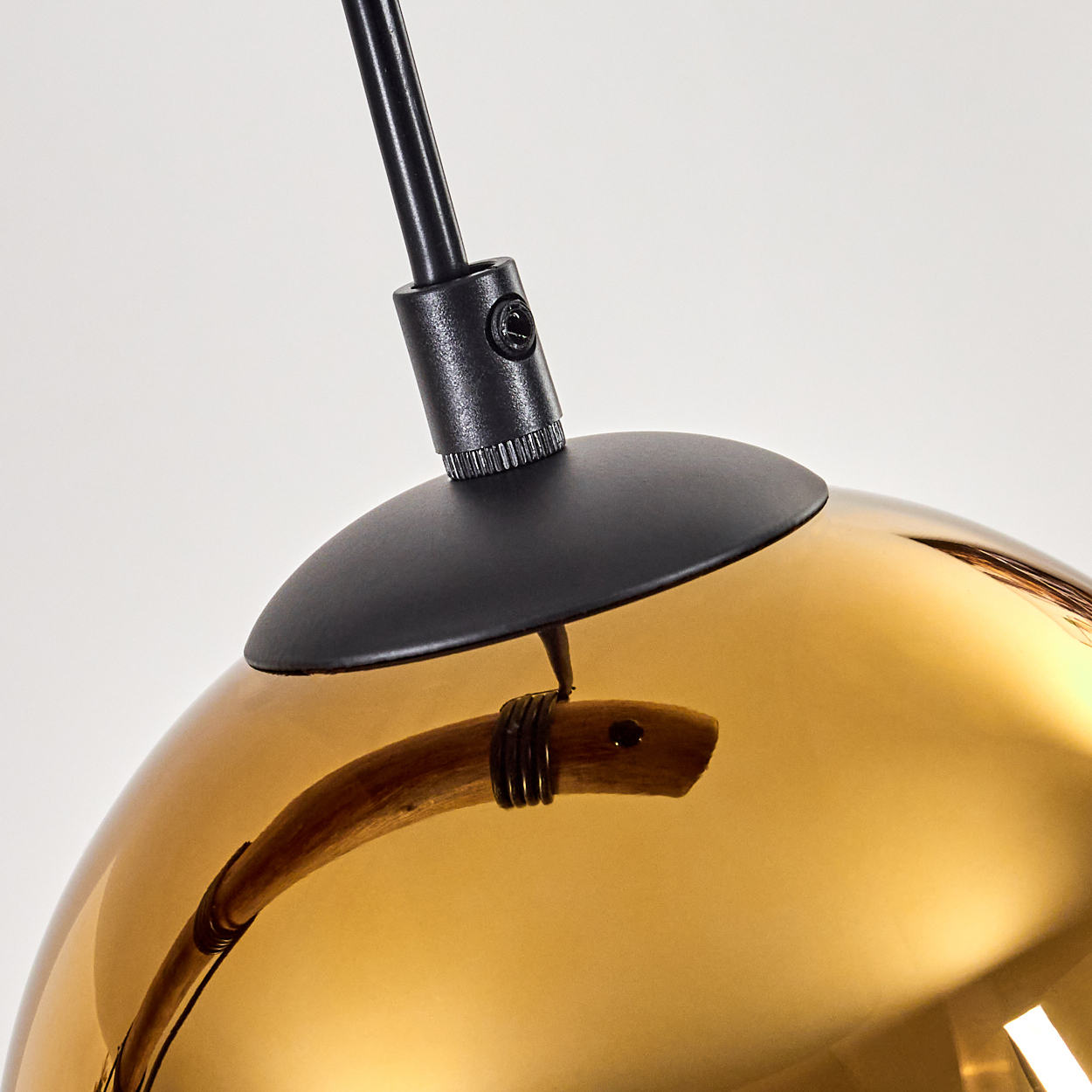Nahaufnahme einer modernen Lampe. Sie hat einen schwarzen Stiel, einen schwarzen Baldachin und eine goldene, reflektierende Glaskugel.
