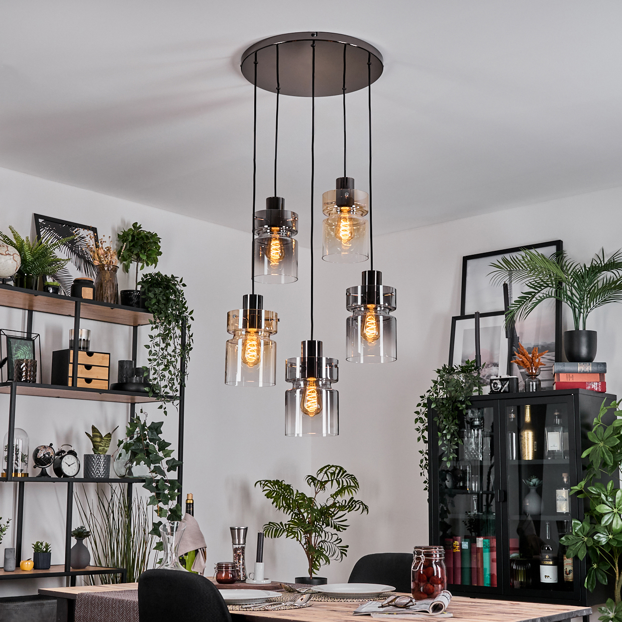 Esszimmer mit Hängelampen, Pflanzen, Holztisch, schwarzen Stühlen, Regalen mit Pflanzen und Dekoration.