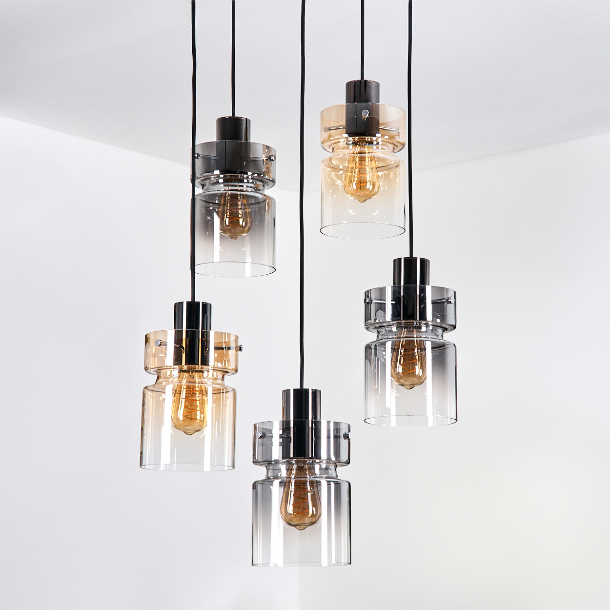 Fünf hängende Pendelleuchten mit Glasschirmen und freiliegenden Glühbirnen vor weißer Wand und Decke.