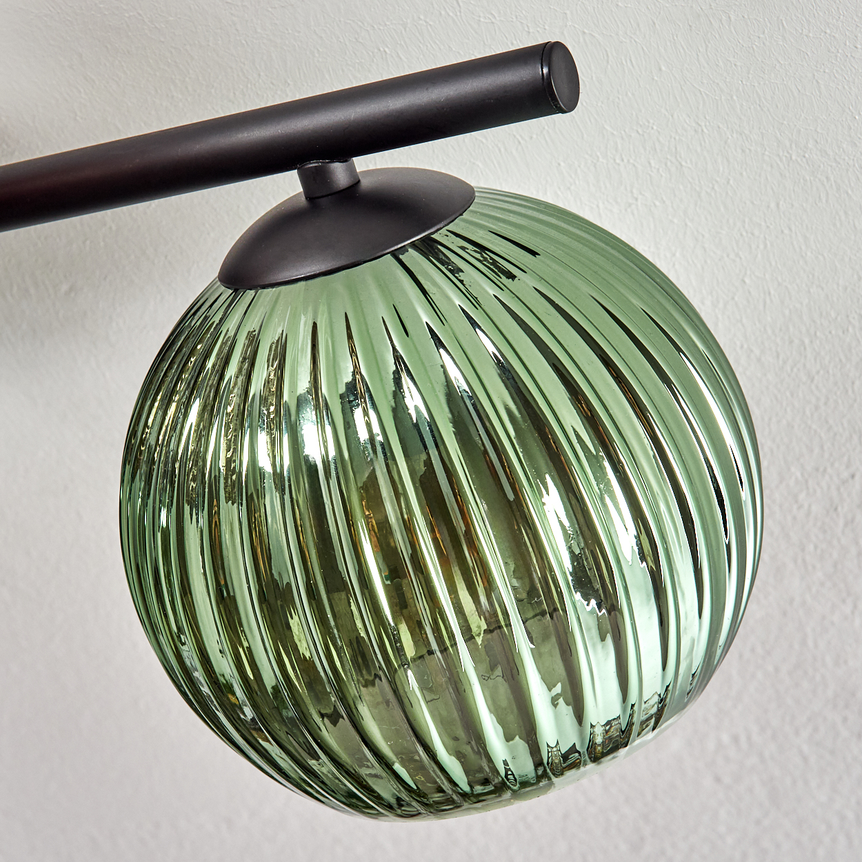 Ein grüner Glasschirm mit vertikalen Rippen. Er ist an einer schwarzen Metallstange und einem schwarzen kreisförmigen Sockel befestigt. Der Hintergrund ist weiß.