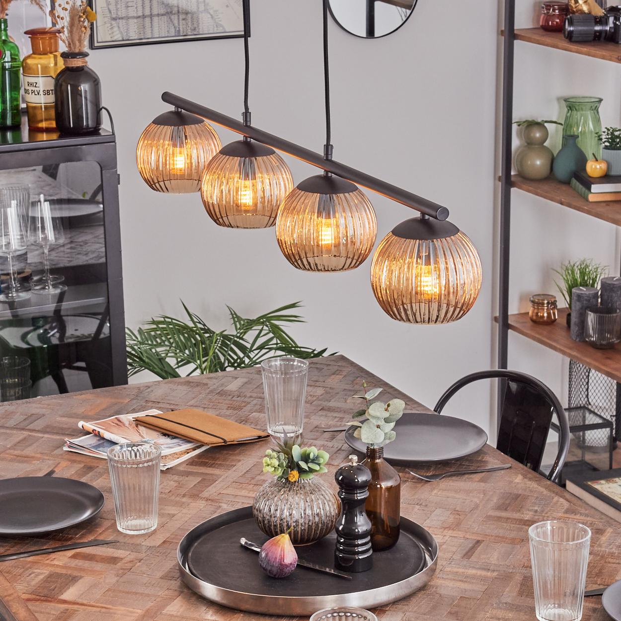 Esszimmer mit Holztisch, vier Kugelleuchten. Tischdeko mit Tellern, Gläsern und einem Tablett mit Feige.
