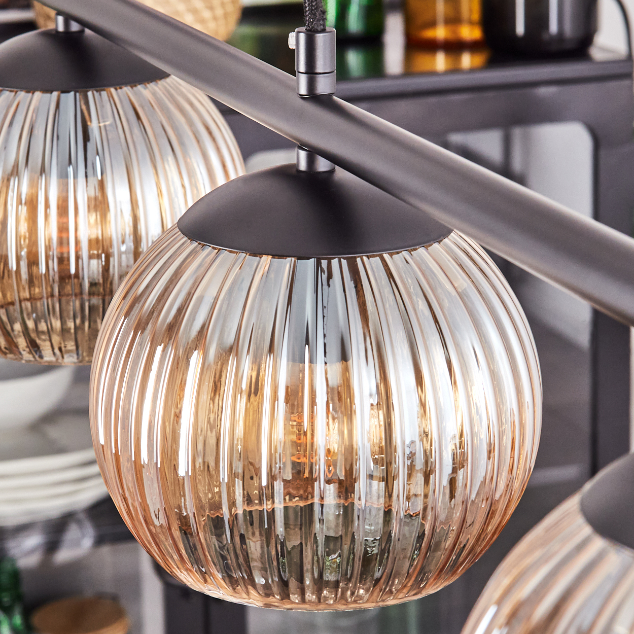 Nahaufnahme einer modernen Leuchte mit drei runden, gerippten Glasschirmen. Die Schirme sind bernsteinfarben, mit schwarzem Metallträger.