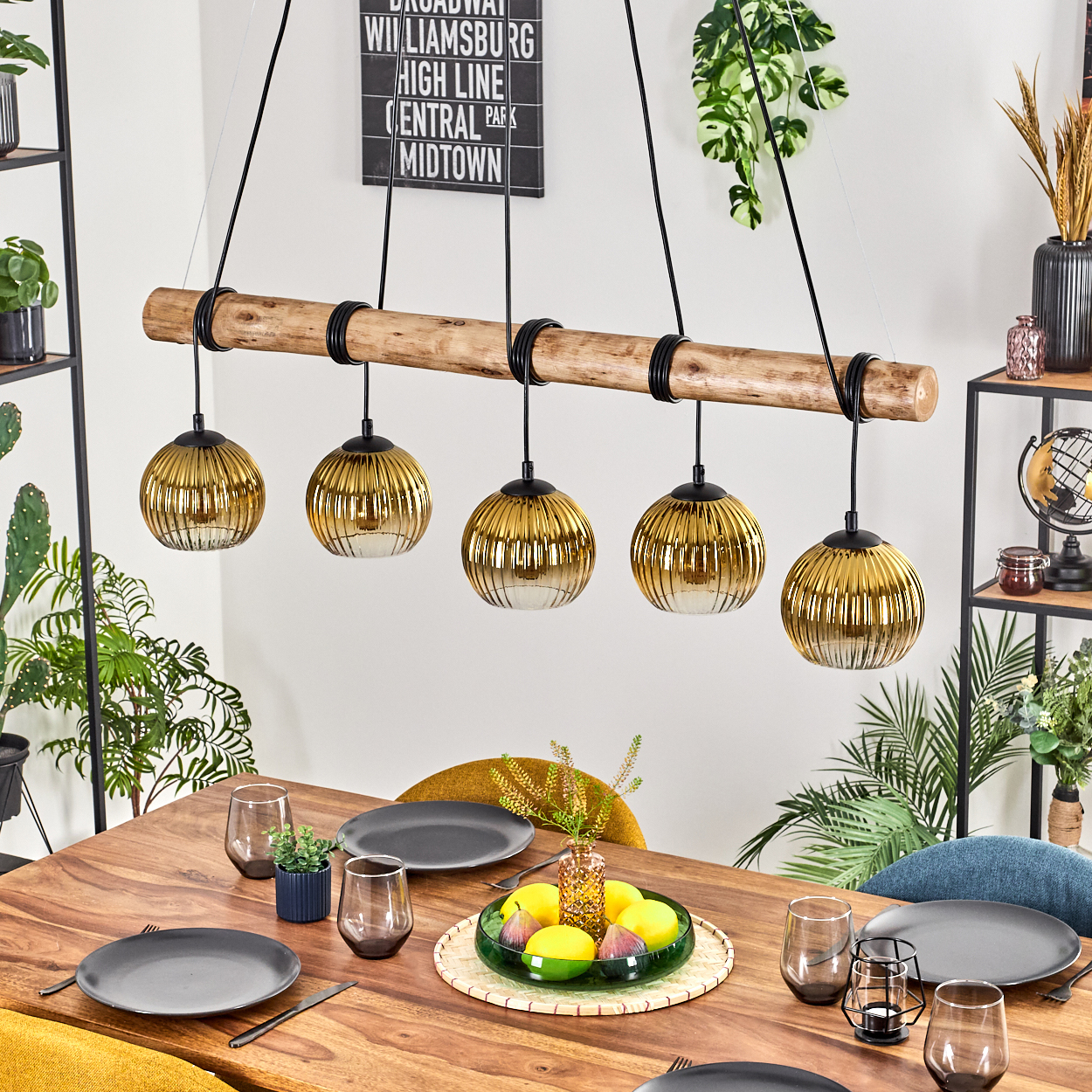Esstisch mit goldenen Lampen, Tellern und Gläsern. Eine Obstschale mit Zitronen und Feigen steht in der Mitte. Pflanzen rahmen die Szene ein.