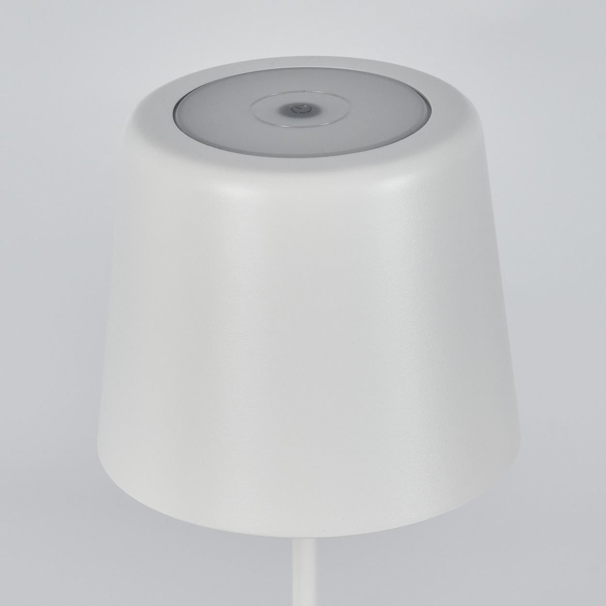 Eine weiße, konische Lampe mit flacher, kreisförmiger Oberseite. Die Oberseite ist heller und der Hintergrund weiß.