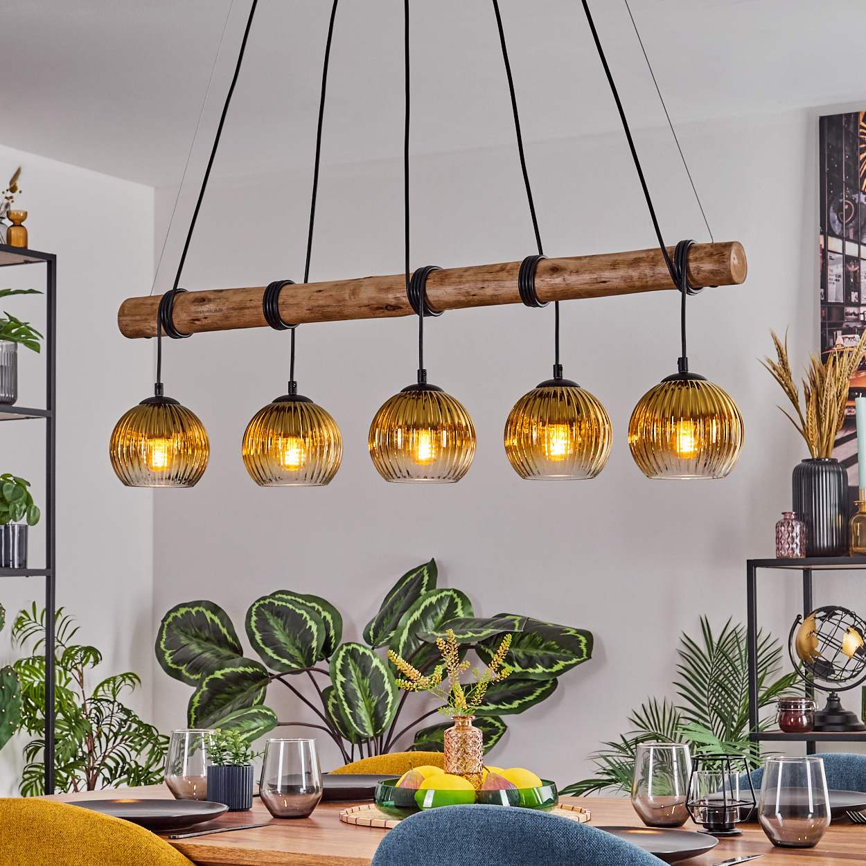 Esszimmer mit Holztisch, Pflanzen und einer Leuchte mit fünf bernsteinfarbenen Glaskugeln.