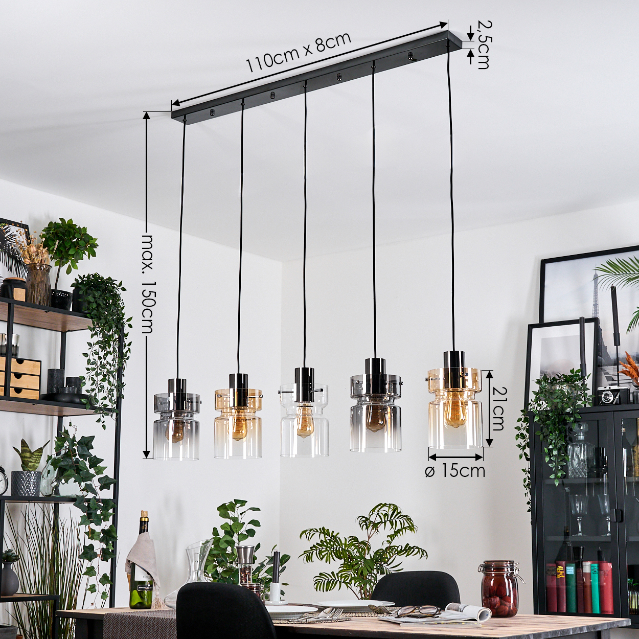 Ein Esszimmer mit einer schwarzen Leuchte mit fünf Glas-Pendelleuchten. Pflanzen, ein Tisch und ein schwarzer Schrank sind ebenfalls sichtbar.