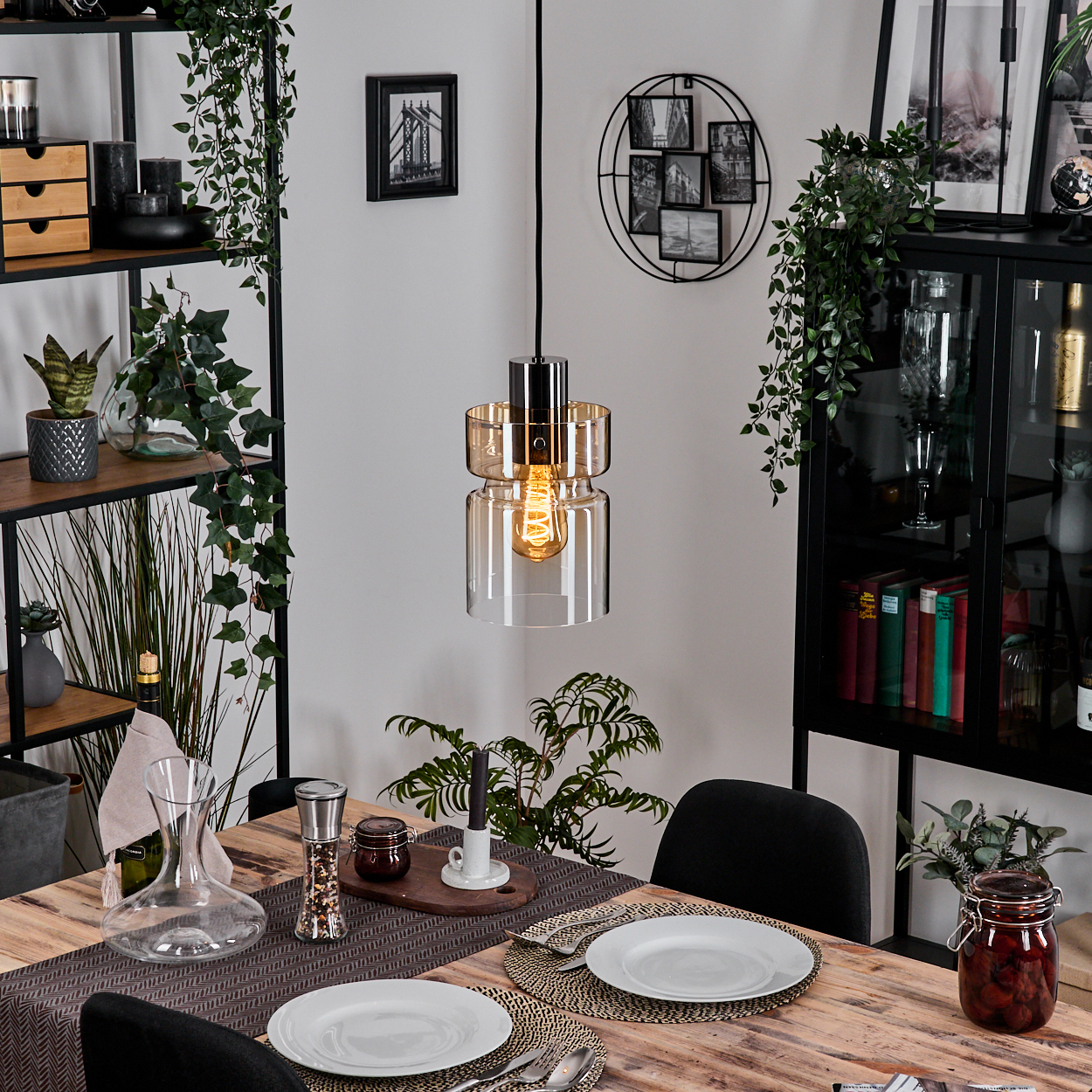Esszimmer mit Holztisch, Tellern, Besteck und Hängeleuchte. Regale mit Deko und Pflanzen.