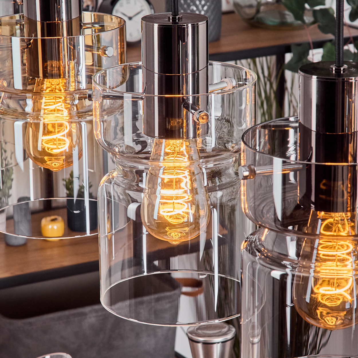 Nahaufnahme von modernen Pendelleuchten mit Glasschirmen und leuchtenden Glühbirnen. Glänzende Metallarmaturen und warmes Licht.