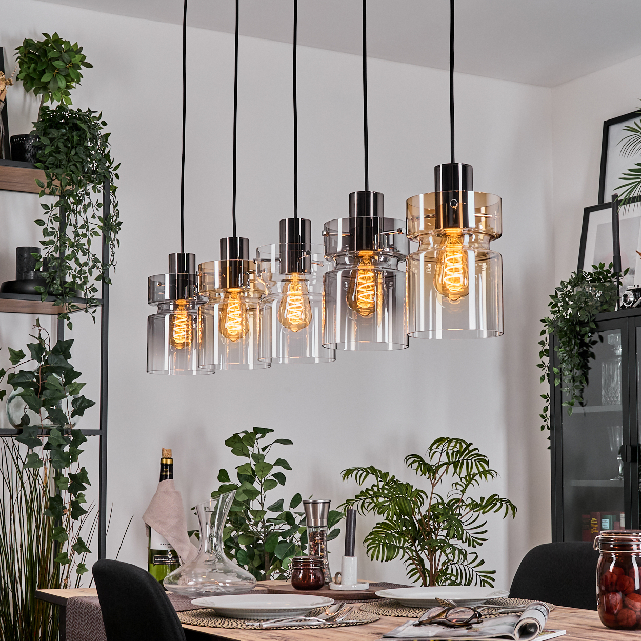 Esszimmer mit Hängelampen. Tisch mit Tellern, Gläsern und Pflanzen gedeckt. Ein Glas mit eingelegten Speisen steht auf dem Tisch.